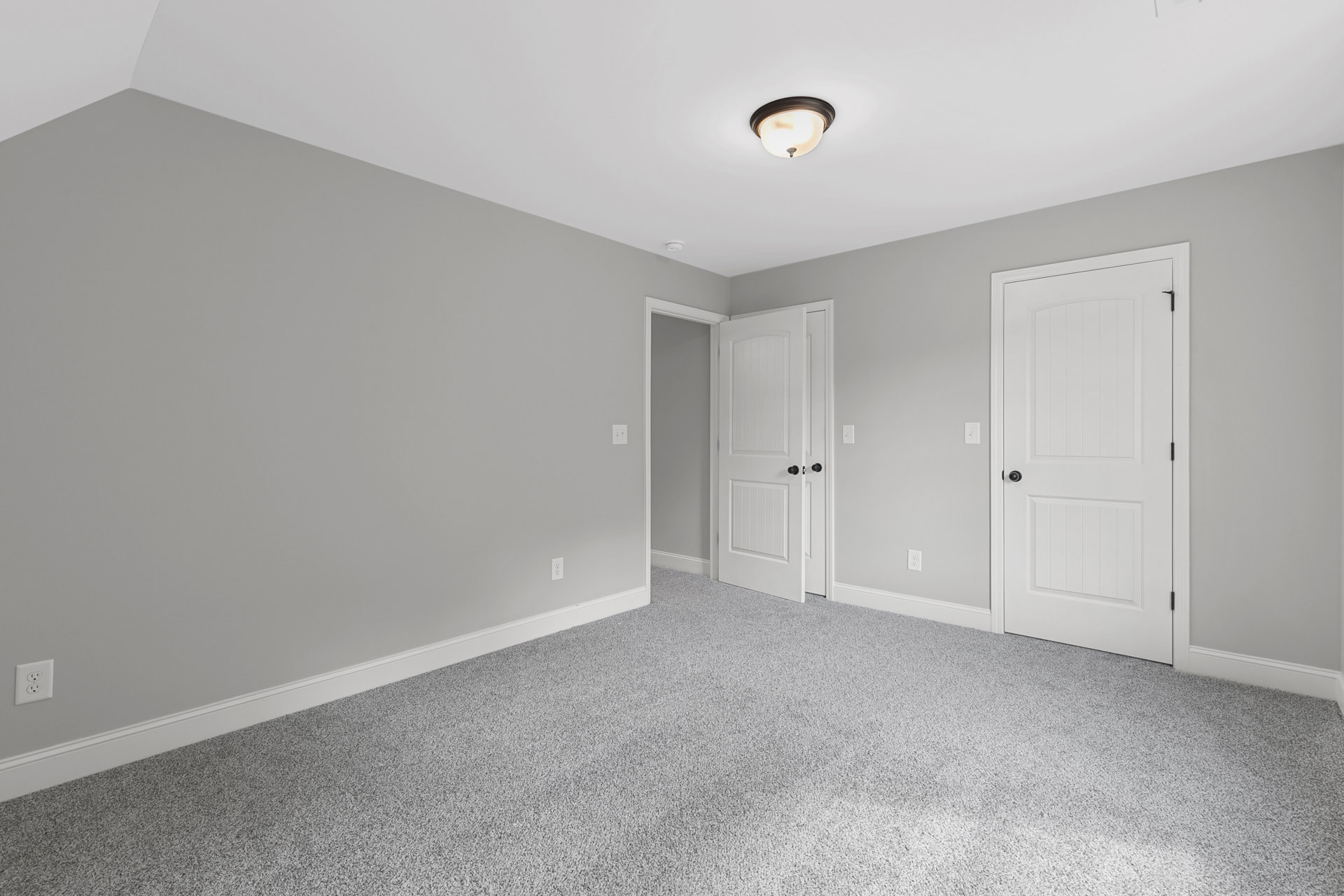 Carpeted room with white walls, white doors featuring black knobs, and a close-up of a light fixture and electrical outlet
