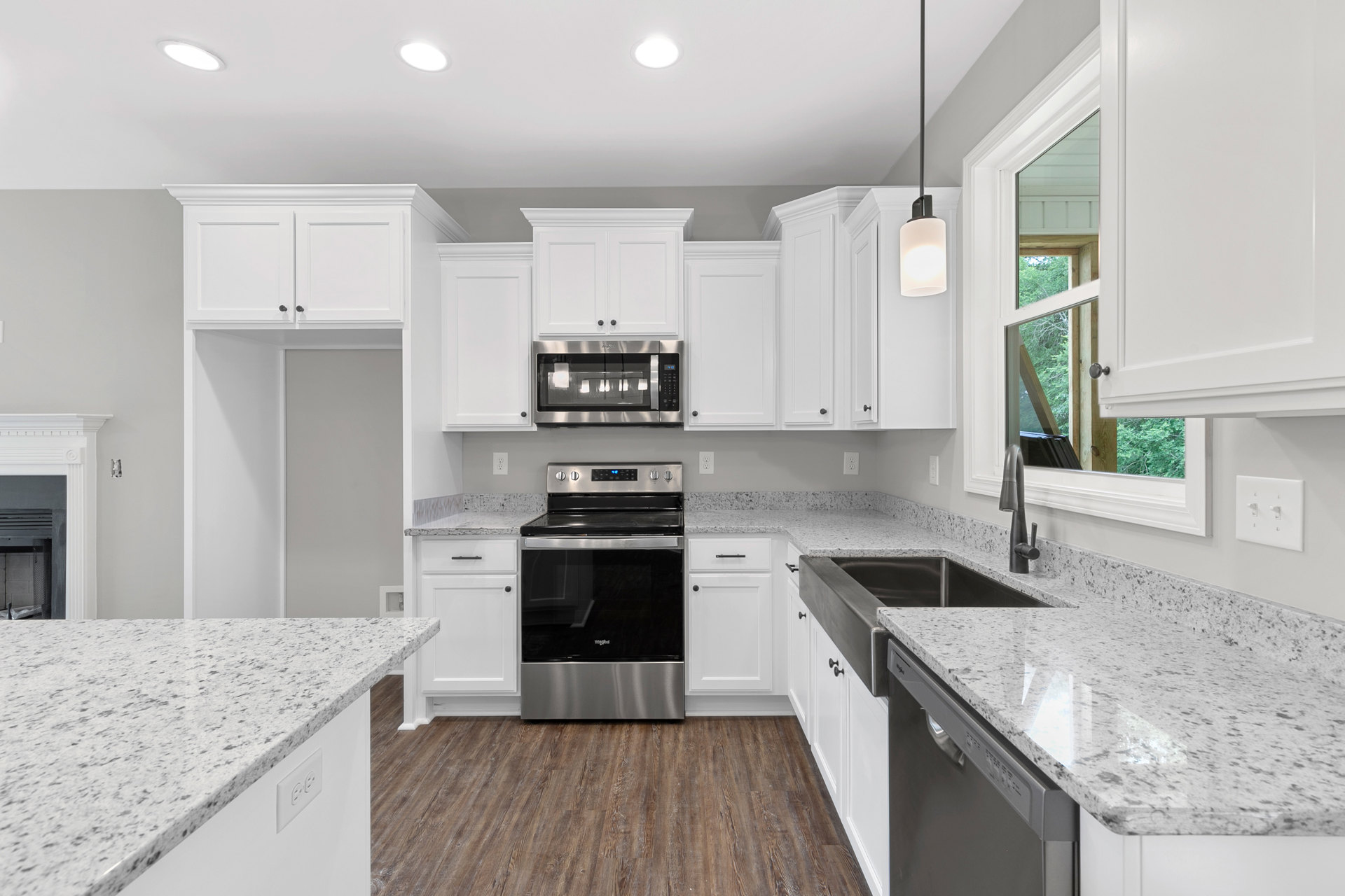 White kitchen cabinets with granite countertops featuring black specks, stainless steel oven and microwave, recessed ceiling light, and undermount sink.