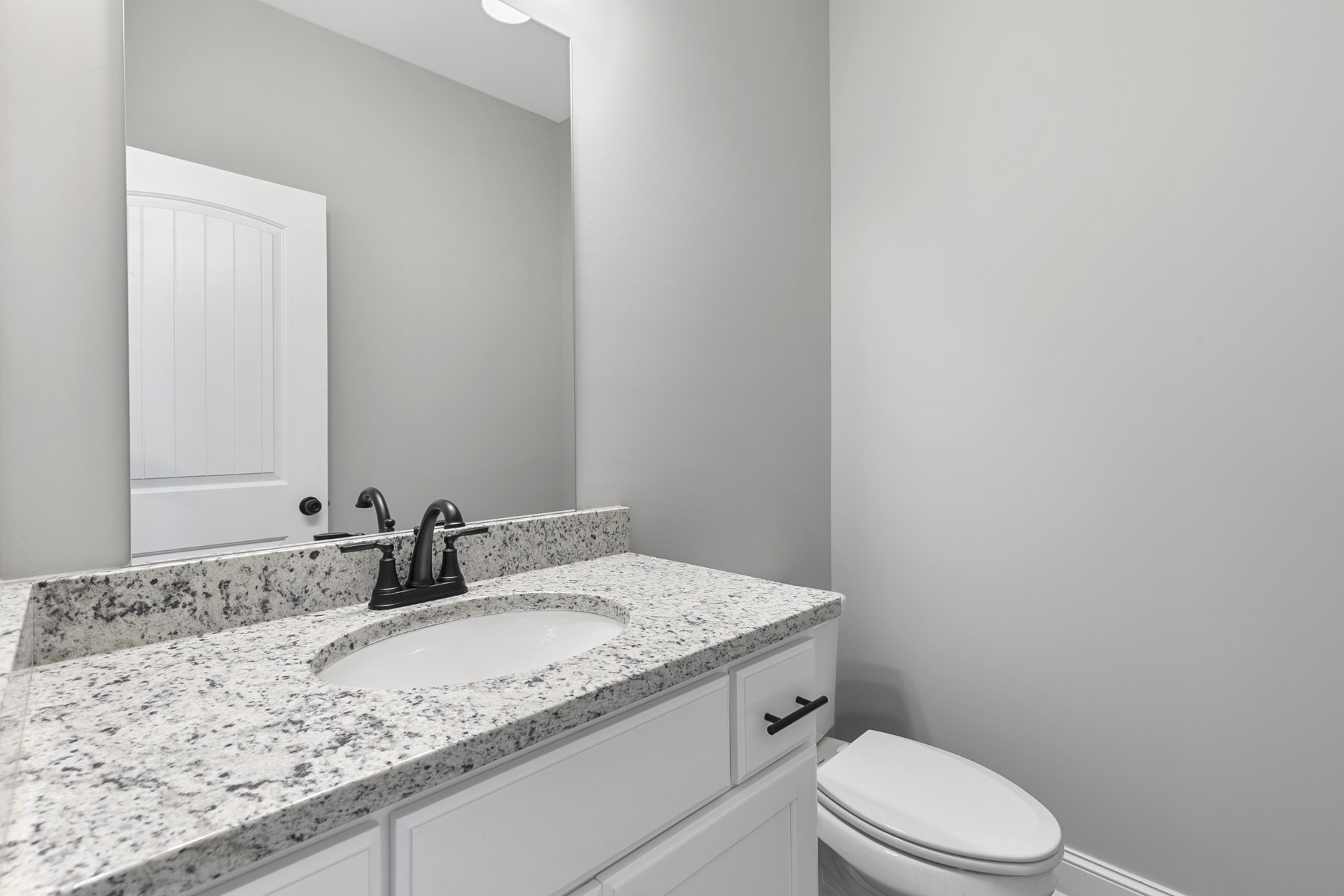 White porcelain sink with chrome faucet, adjacent to a white toilet, light-colored tile flooring, vertical paneled door, wall-mounted mirror above the sink