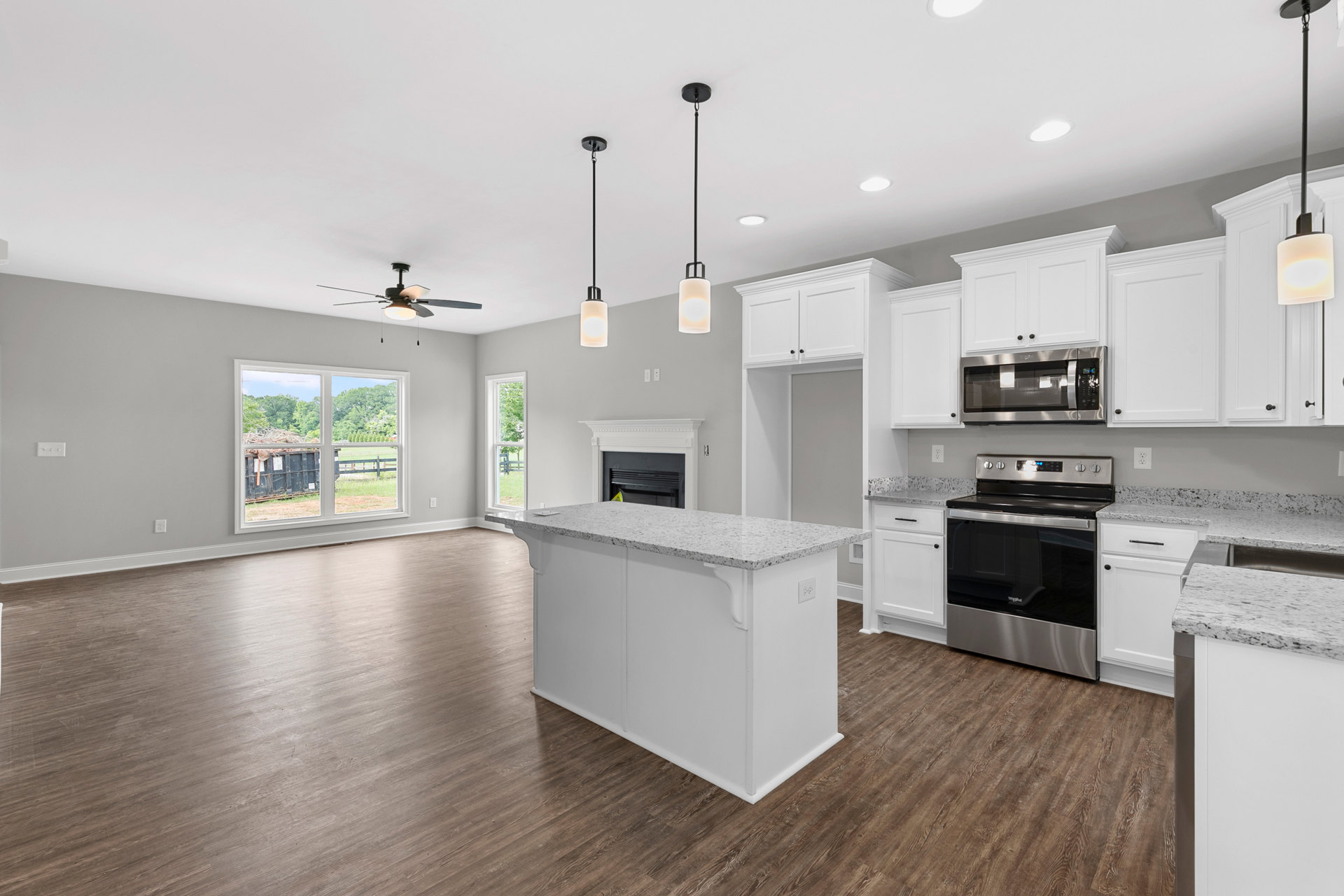 Open-concept kitchen and living room featuring white cabinetry, wood flooring, white kitchen island, black glass stove, built-in microwave, and white countertops with a modern