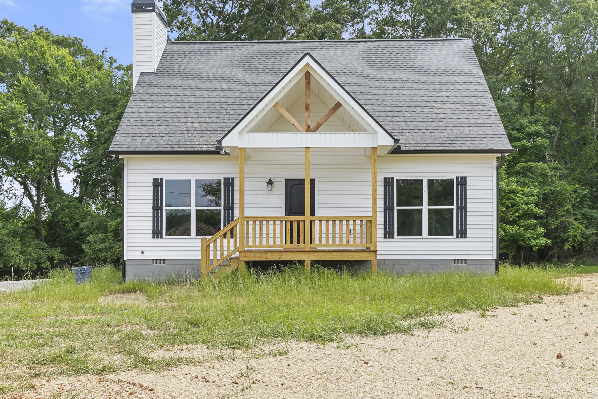 Two-story home with covered front porch, wooden bench, white-framed windows, driveway, and landscaped grass with tall plants and wood chips.