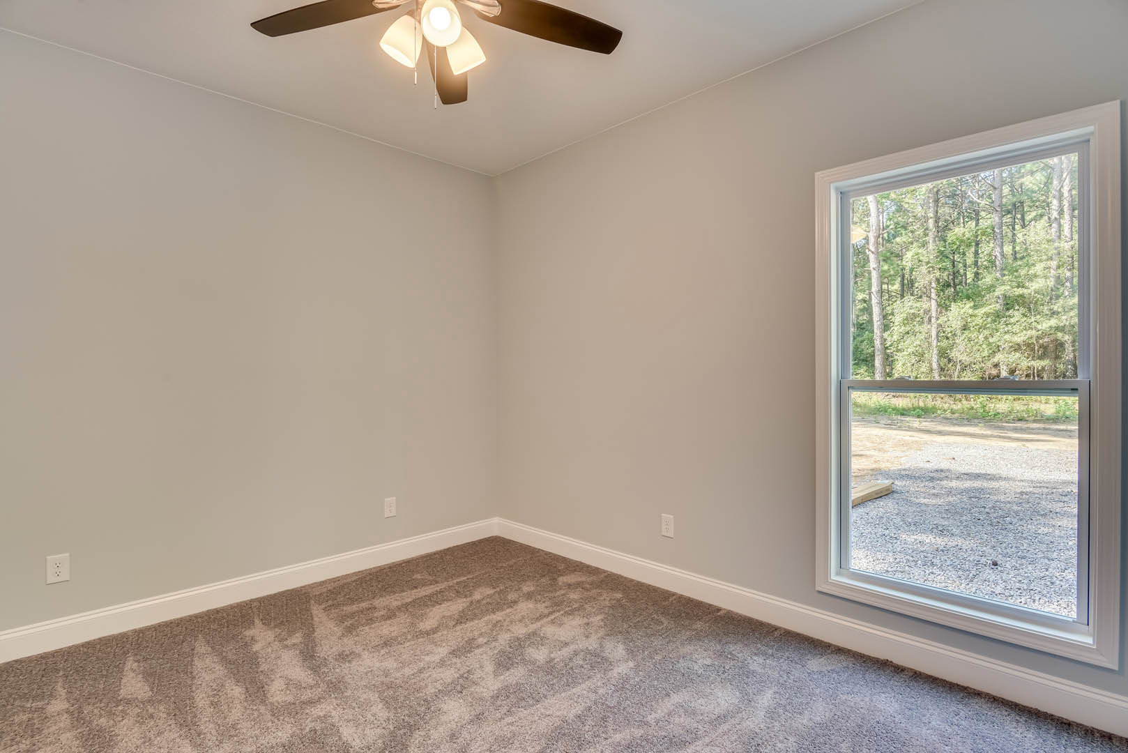 Carpeted bedroom with white walls, ceiling fan with light fixture, large window overlooking trees, crown molding along ceiling.