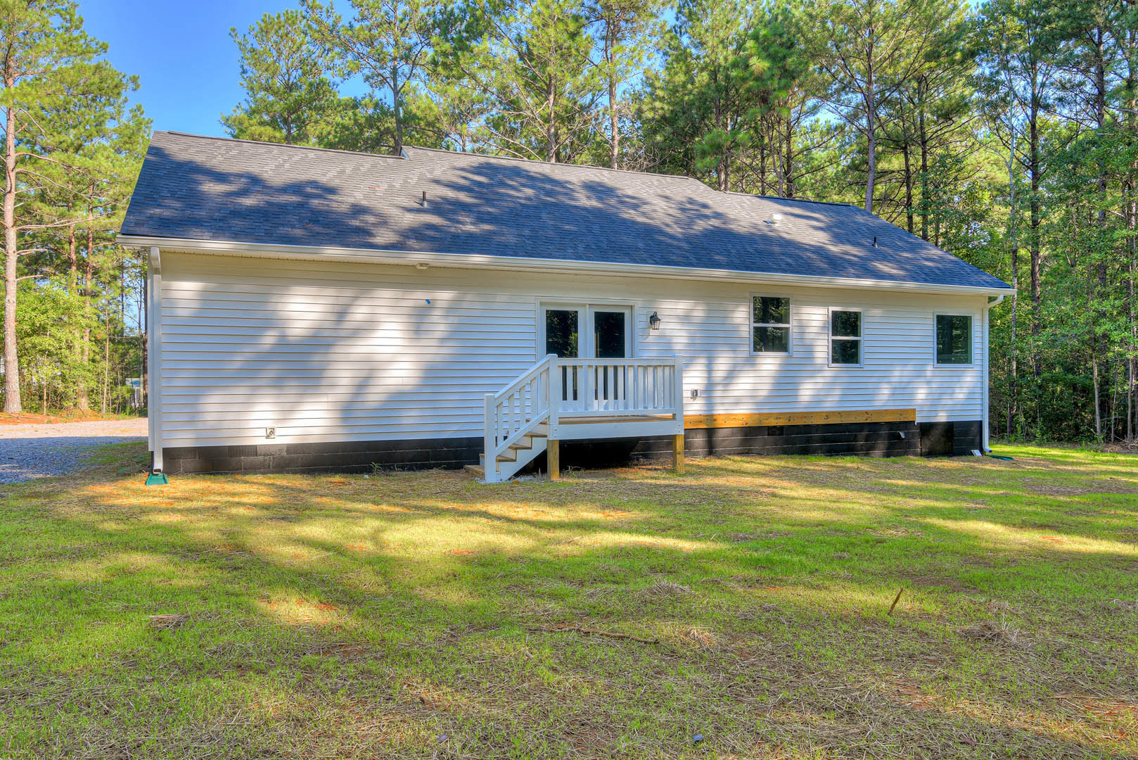 White cottage-style home with covered porch, white railings, wooden steps leading to grassy yard, large window with white frame, mature tree and plants in outdoor setting