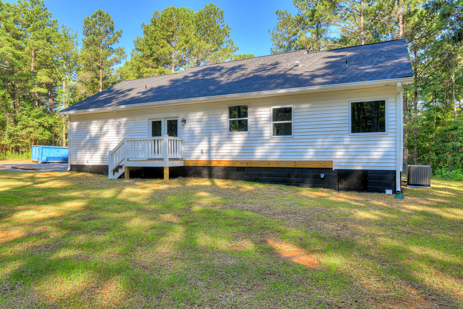 Two-story house with gray siding, front porch featuring a white bench, wooden deck, manicured lawn, and mature trees in the background
