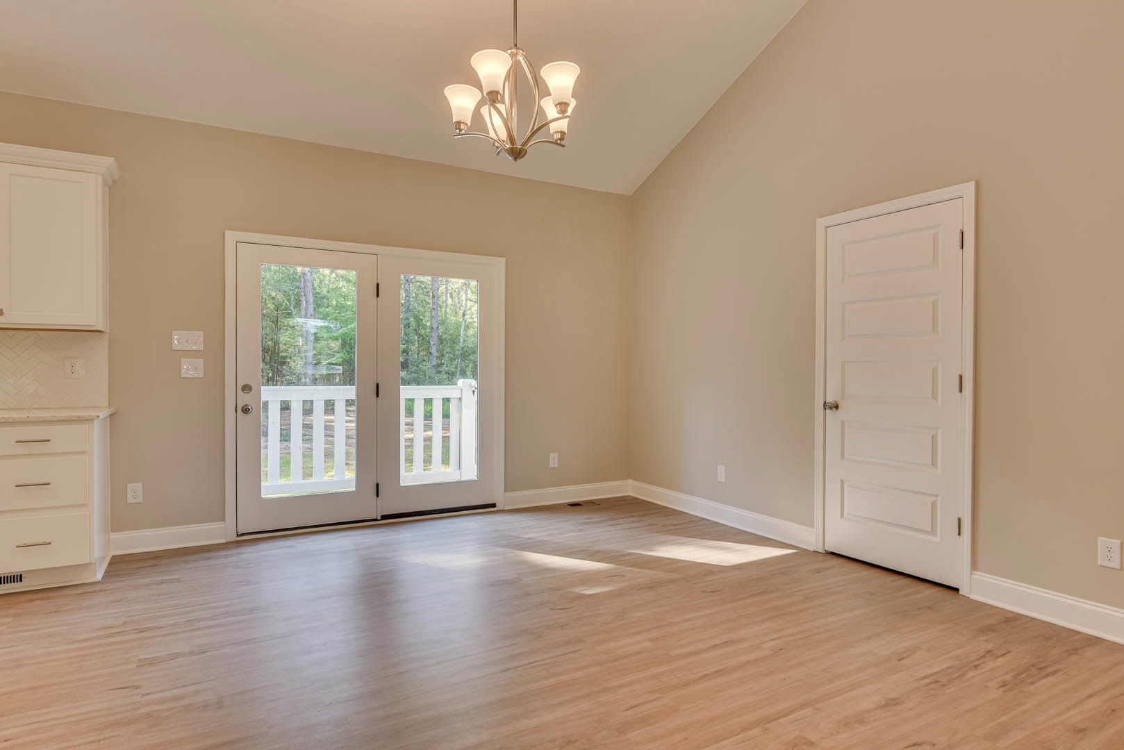 Hardwood floor in a bright room with white double doors featuring glass panes and silver handles, chandelier overhead, white cabinetry and drawers along the kitchen wall