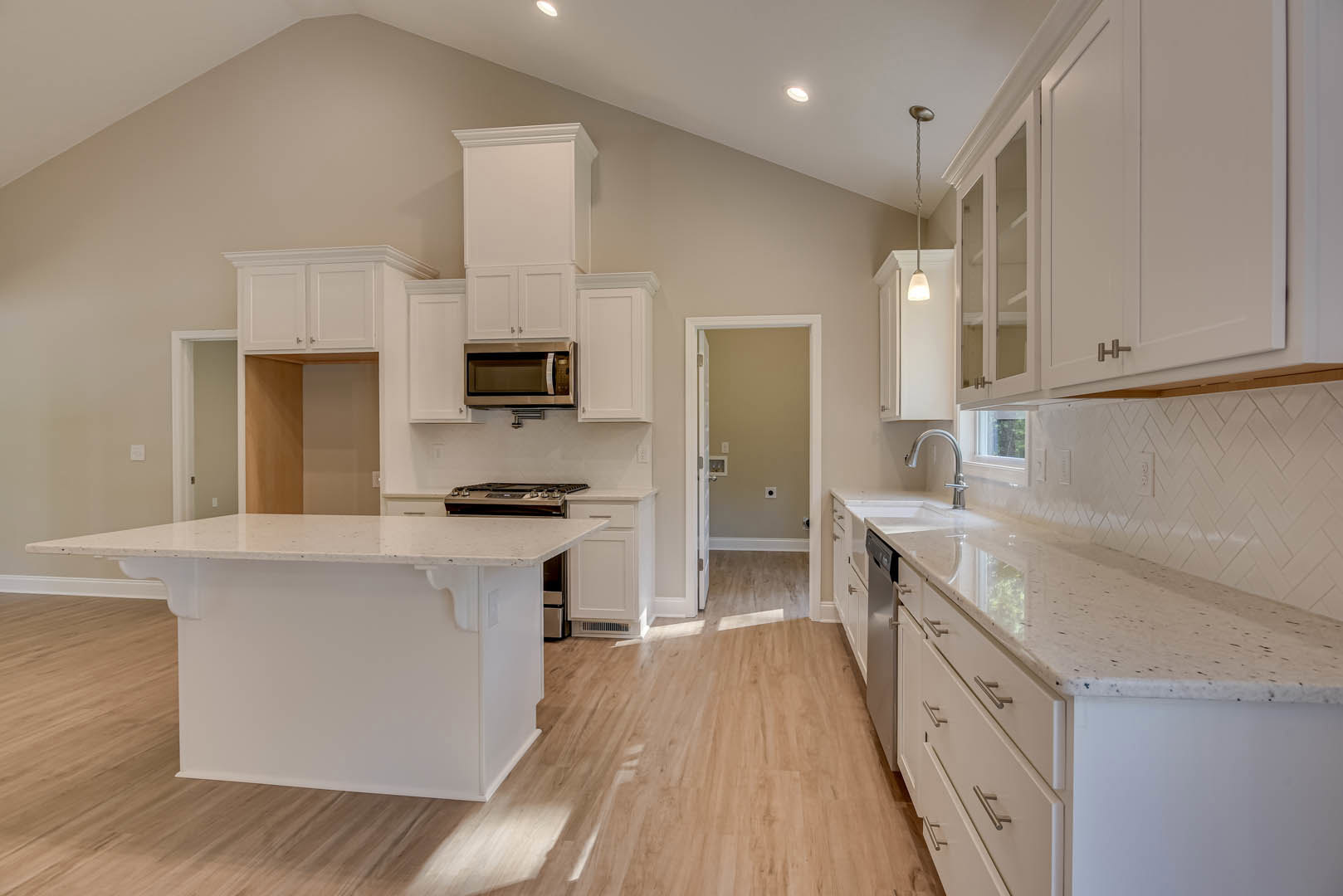White kitchen cabinets with sleek white countertops, wood flooring, open microwave door, stainless steel faucet, and white-framed door in a modern kitchen interior.