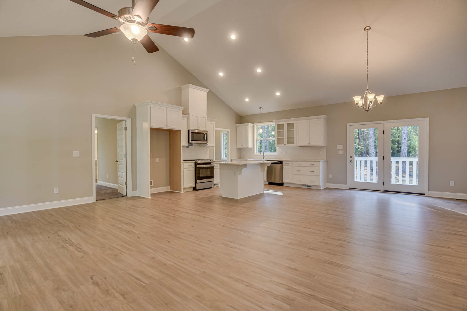 Spacious open floor plan featuring hardwood flooring, kitchen with stainless steel appliances including microwave and oven, dining area, glass-panel double doors, and ceiling fan