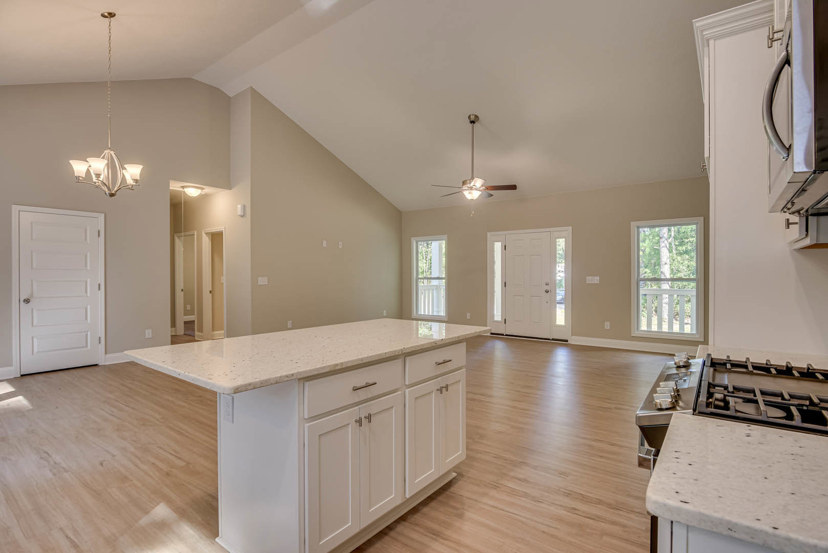 Open-concept kitchen and living room featuring a ceiling fan, marble kitchen island, white cabinetry, stainless steel appliances, white doors with silver handles and glass panels