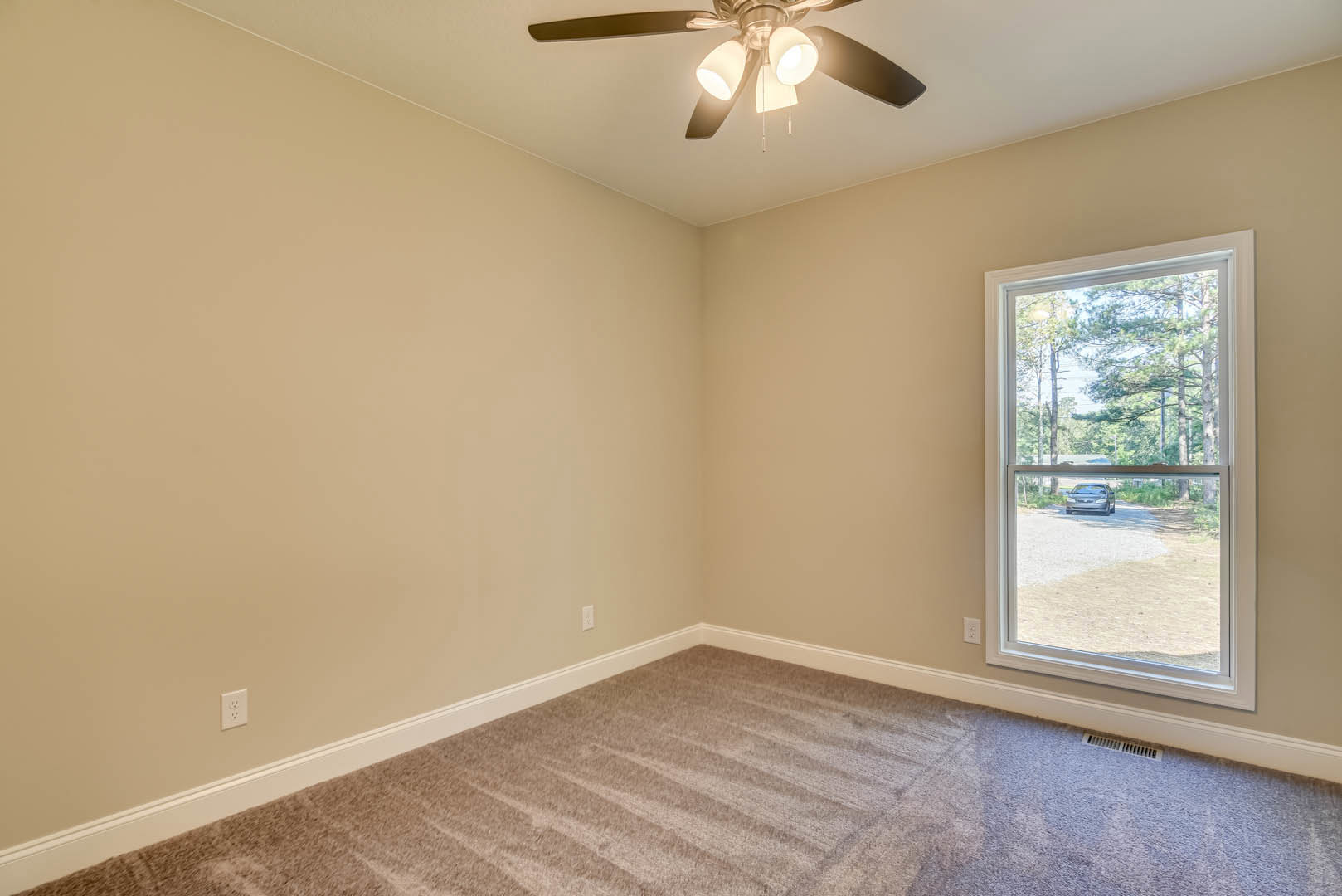 Carpeted bedroom with white walls, ceiling fan with lights, large window overlooking green trees, crown molding along ceiling.