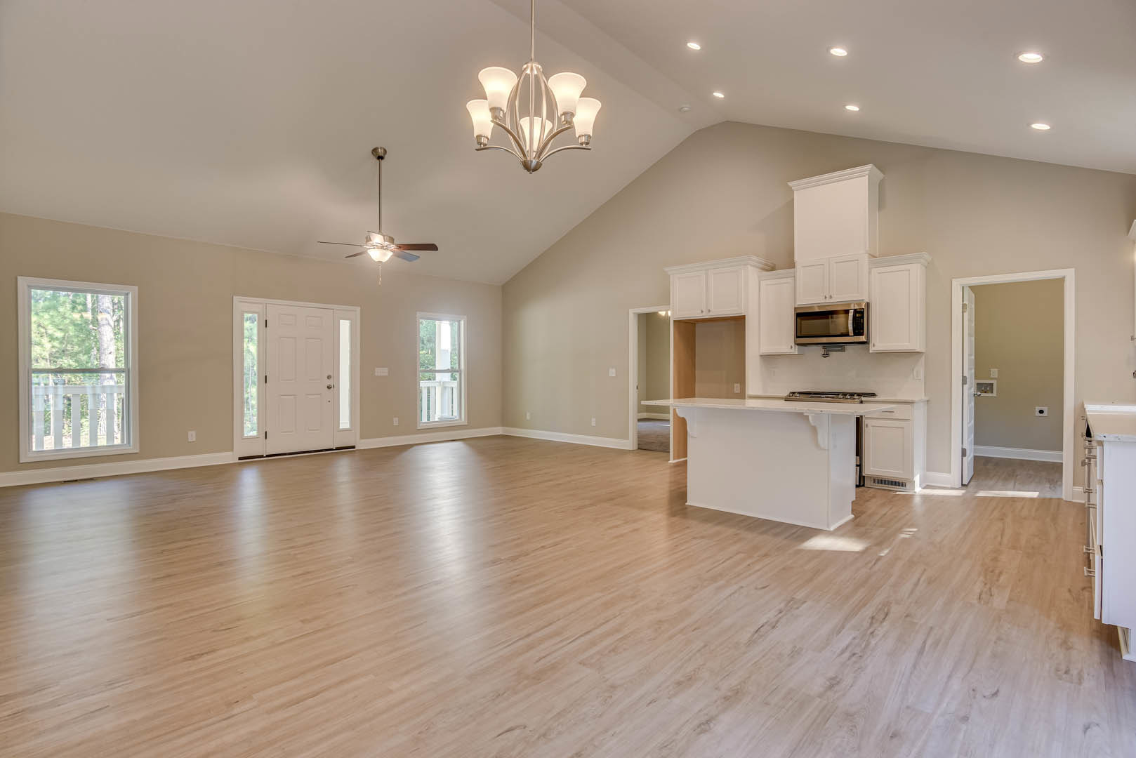 Spacious open floor plan featuring a kitchen with white cabinetry, hardwood flooring, large window with white frame and railing, modern light fixture with five bulbs, close-up of