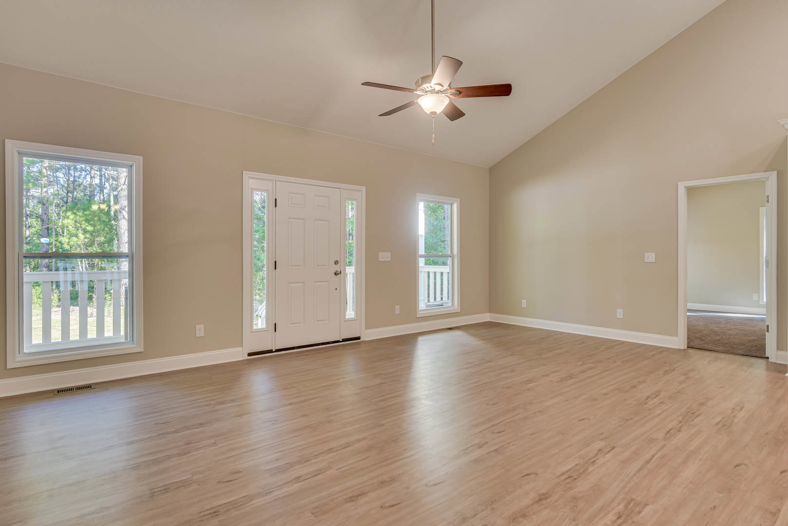 Ceiling fan with light fixture, hardwood floor, large window showing trees, white door with glass panels, white door frame, neutral walls