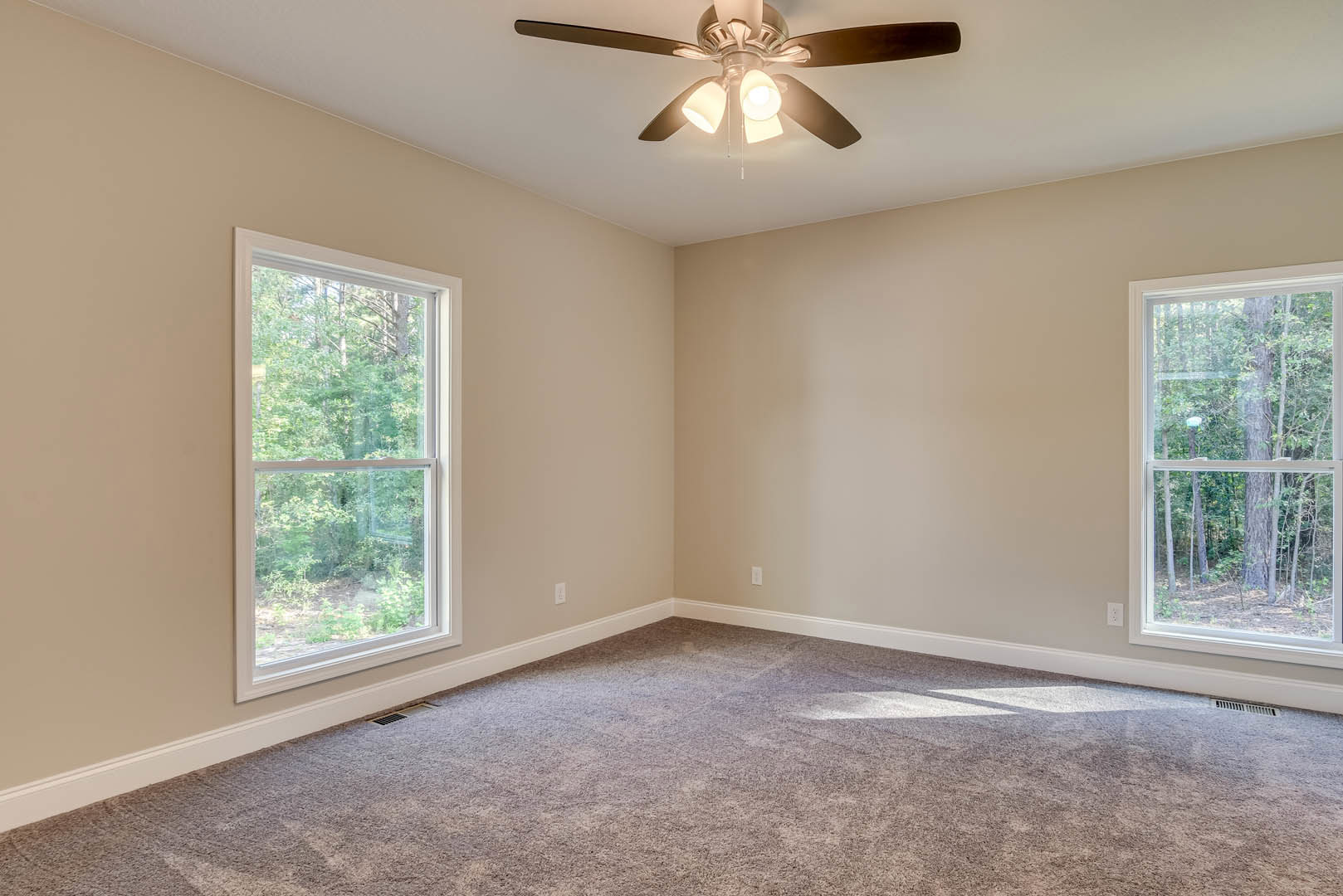 Carpeted room with white walls, ceiling fan with lights, large window overlooking trees, crown molding along ceiling