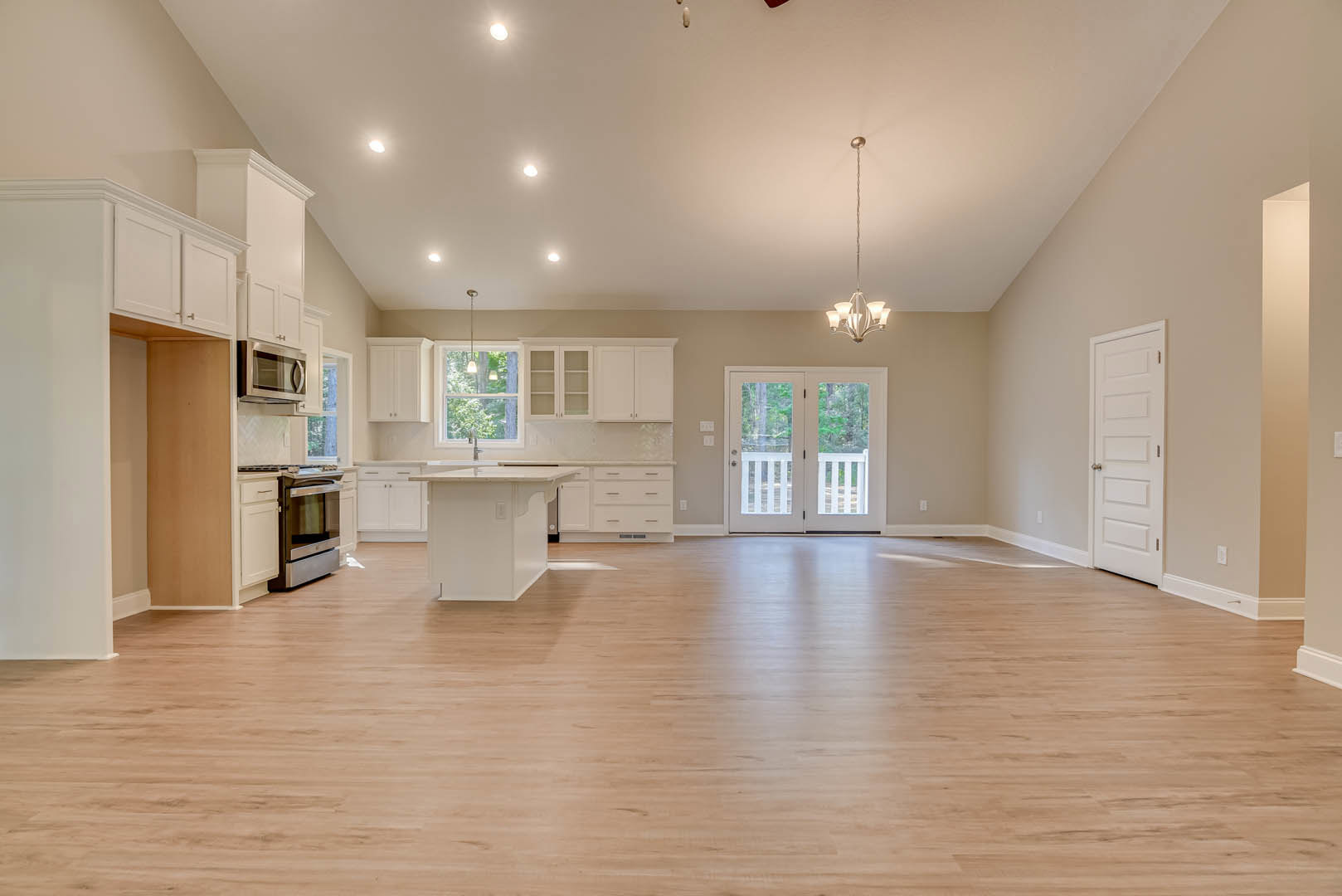 Spacious open-concept interior featuring hardwood flooring, white kitchen island with cabinetry, glass-paneled double doors, and white doors with silver hardware