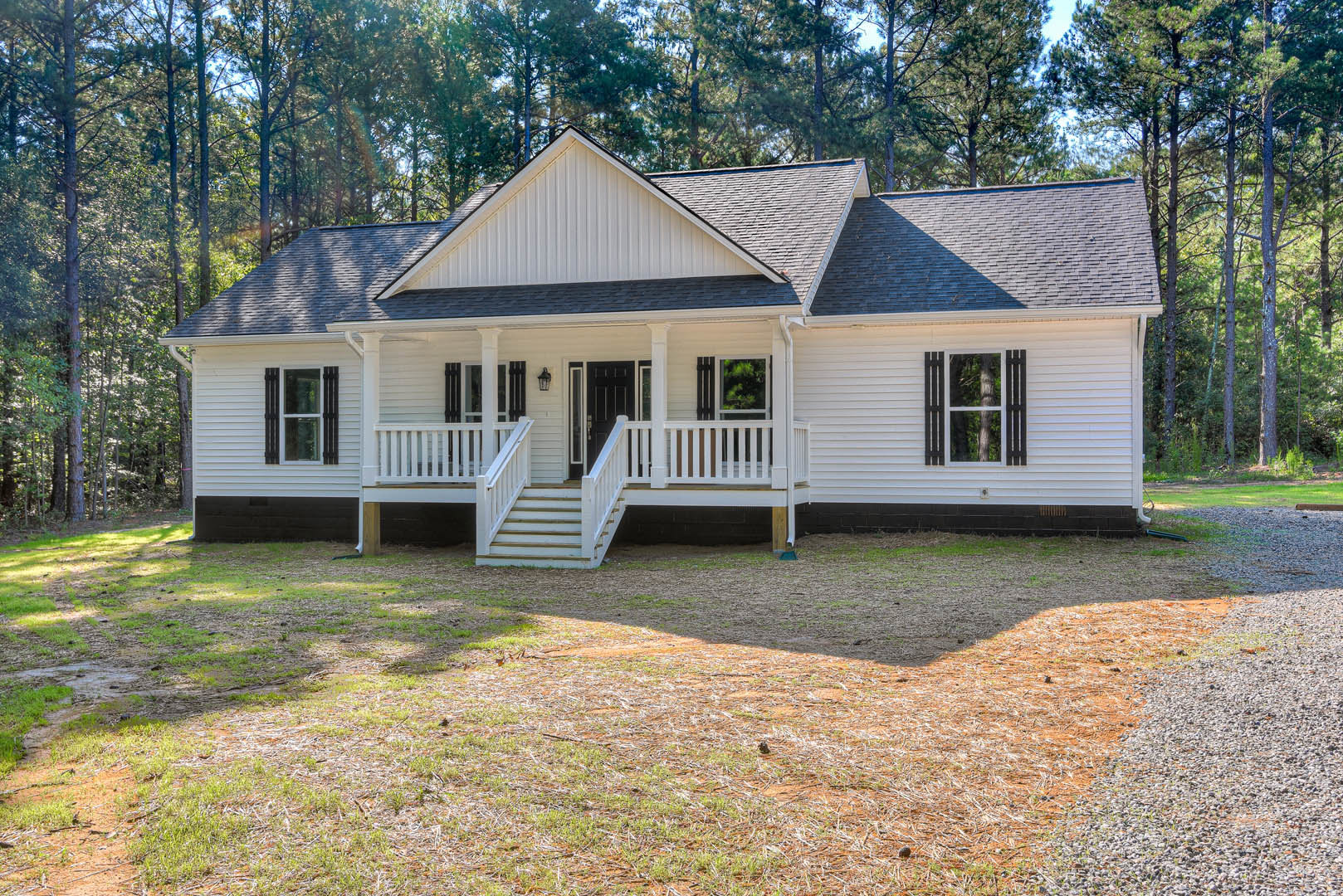 White siding house with black front door, covered porch, white framed windows, grassy yard, and mature trees in the background