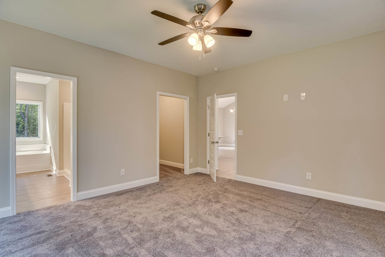 Carpeted room with white door, ceiling fan with lights, window showing tree outside, white door frame, corner shelving, light-colored walls and molding