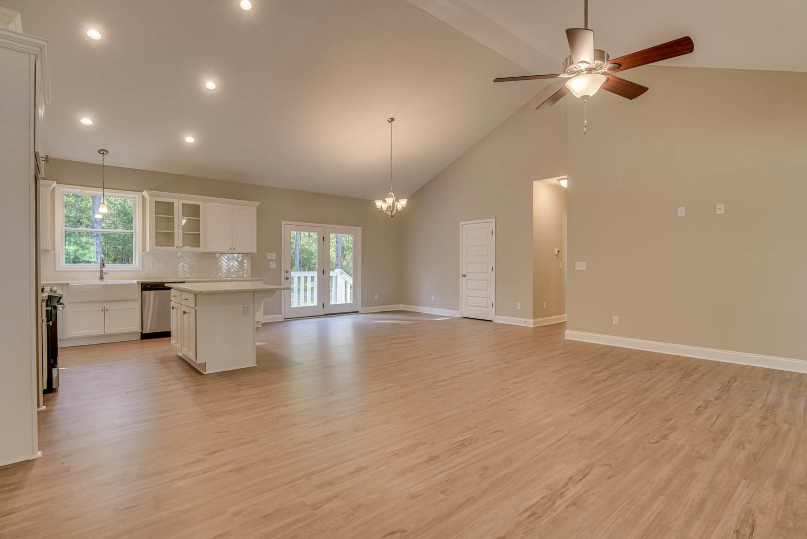 Spacious open floor plan featuring hardwood floors, a ceiling fan with light, white kitchen island with drawers, double glass-paneled doors, and a white door with silver knobs
