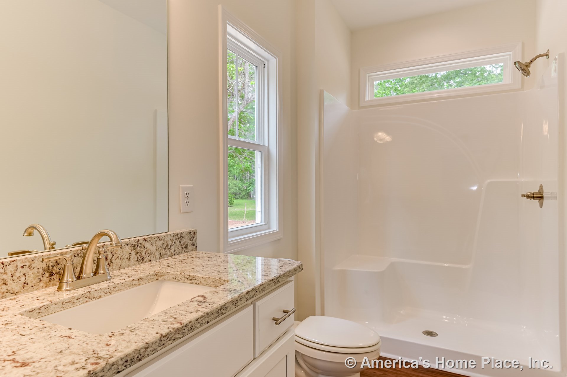 Granite countertop with single sink and brushed nickel faucet atop white shaker cabinets, walk-in shower with built-in bench and glass door, double windows with decorative trim