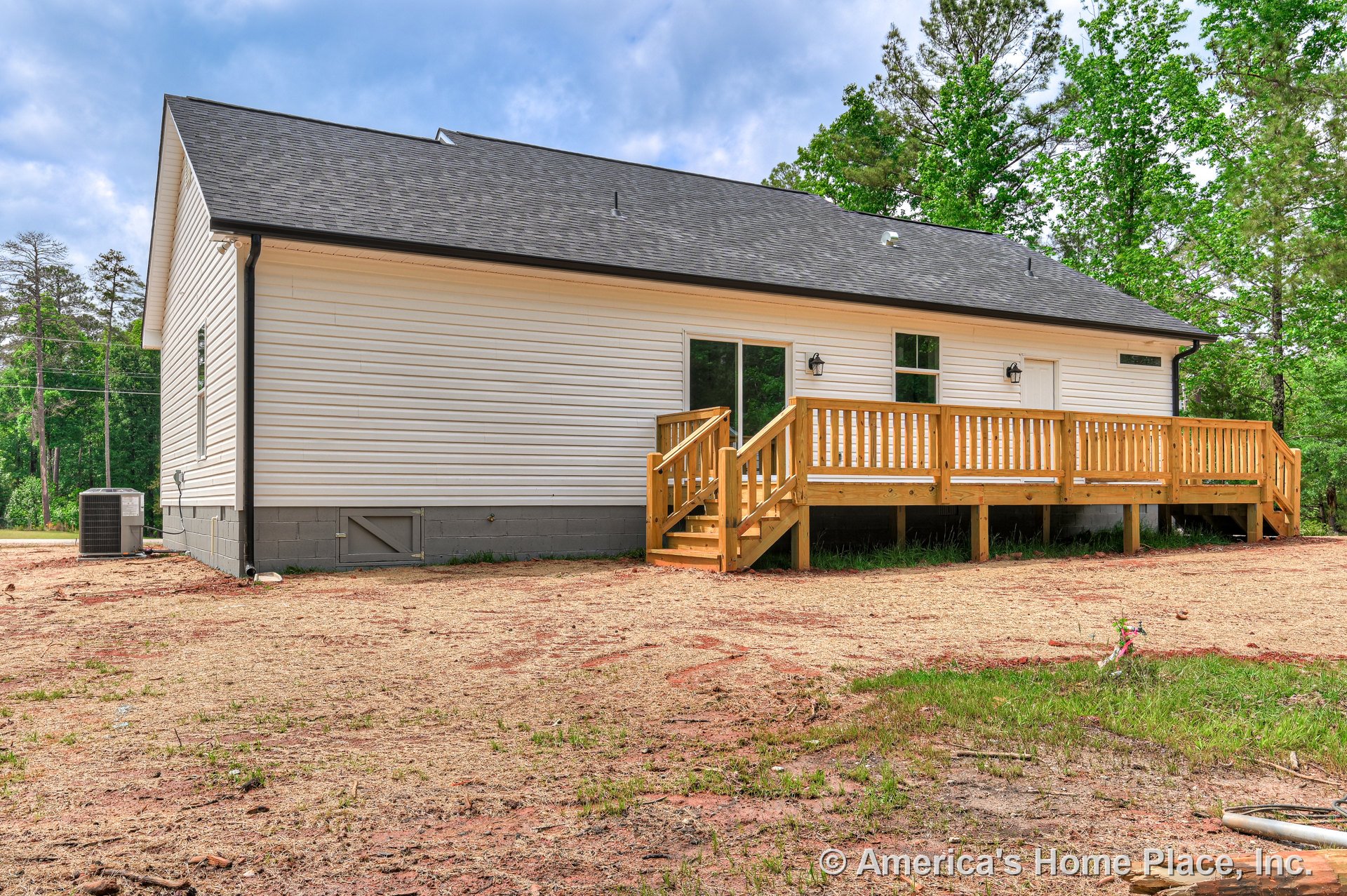 Newly built wooden rear deck with steps and railings, exterior vinyl siding, sloped shingle roof, concrete block foundation, sliding glass door, outdoor wall-mounted lighting, and