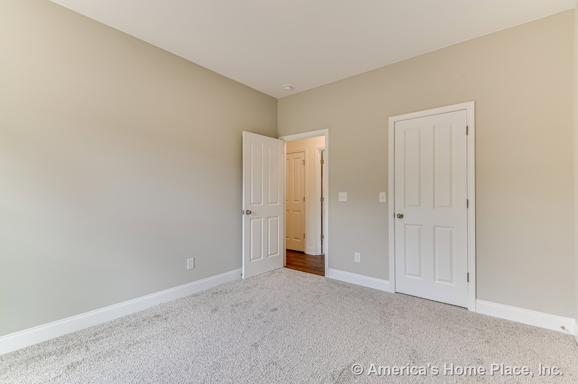 Bedroom with light beige walls, white baseboards and trim, carpet flooring, white paneled closet and entry doors, simple ceiling, visible wall outlets, and hallway access.