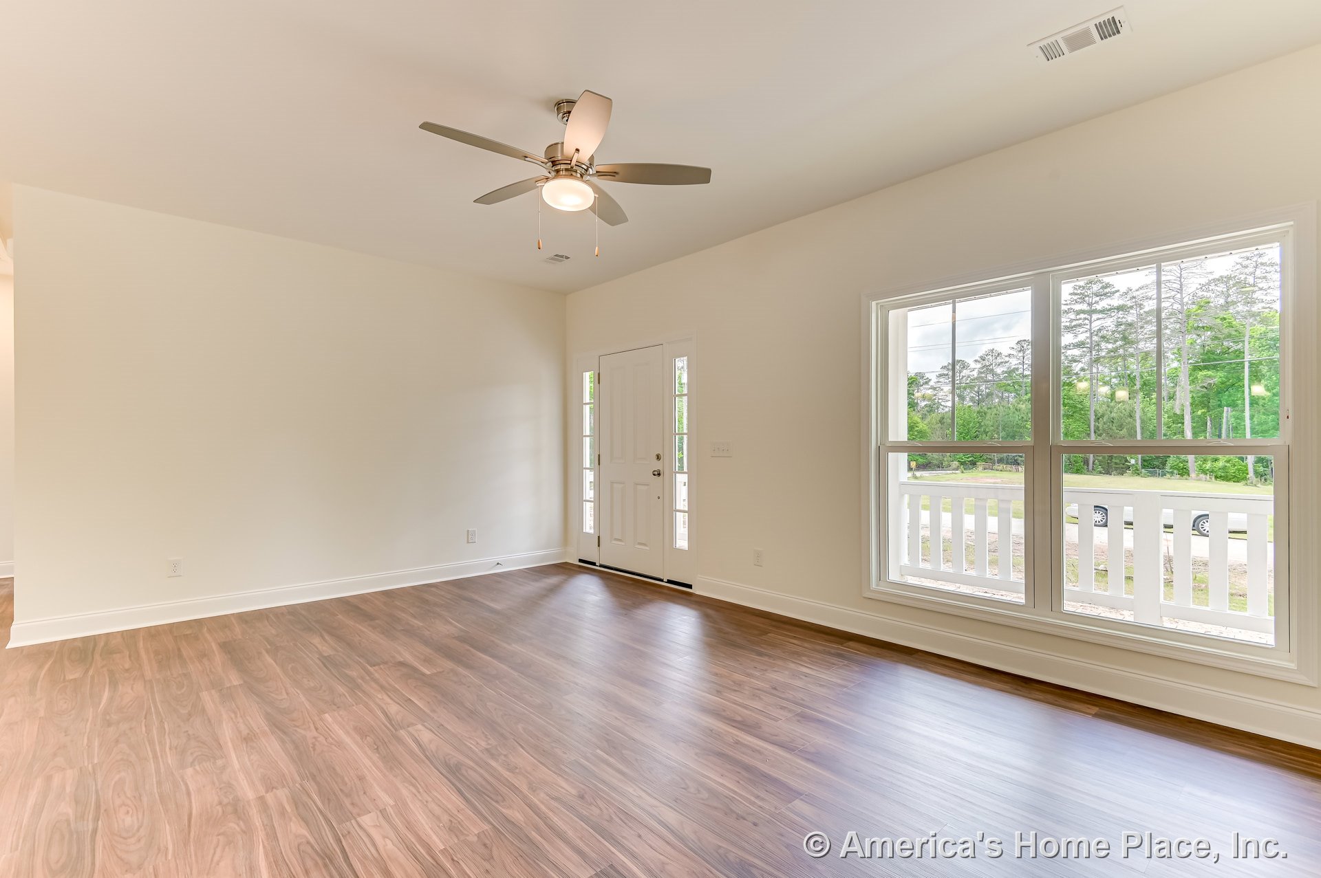 Living room with wood-look plank flooring, ceiling fan with integrated light, large double windows, white trim and baseboards, entry door with sidelights, and neutral wall color.