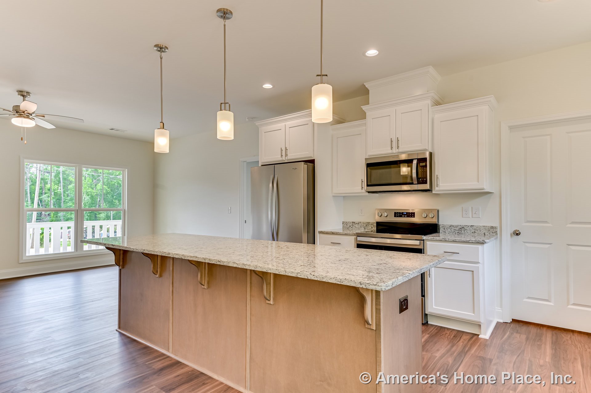 Spacious kitchen with large granite island, white shaker cabinets, stainless steel refrigerator and built-in microwave, pendant and recessed lighting, wood-look flooring, double