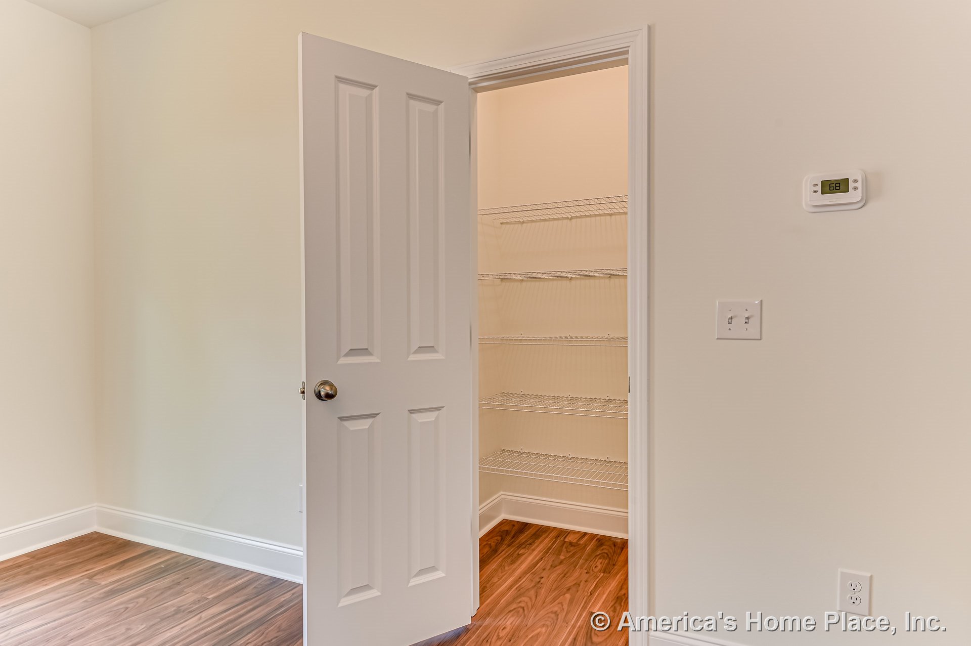 Closet with white paneled door, multiple wire shelves, wood-look vinyl plank flooring, light painted walls, baseboard trim, wall thermostat, and electrical outlet.