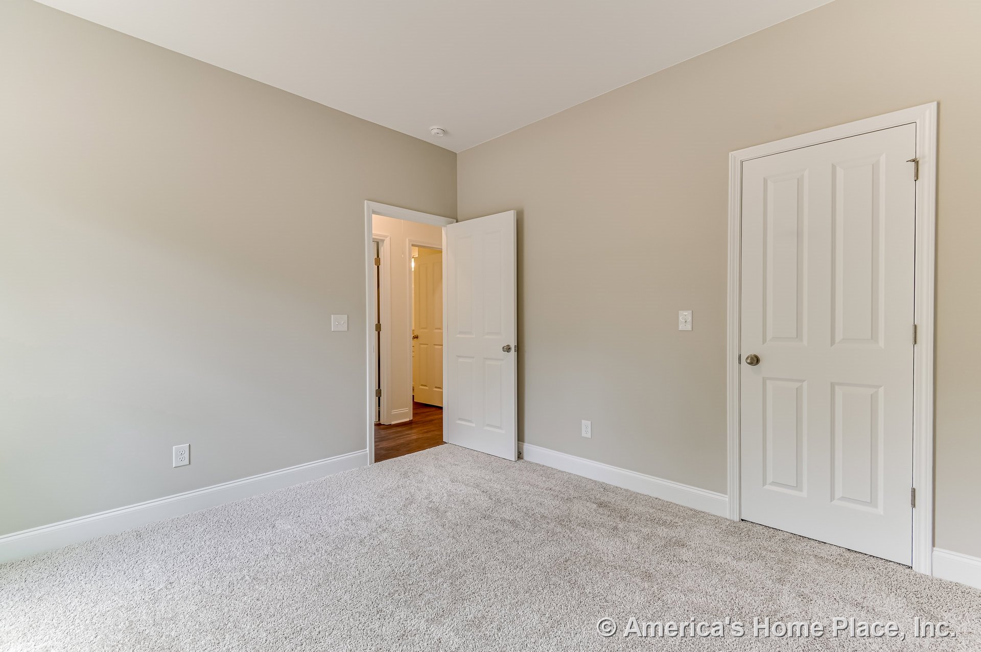 Bedroom with light beige carpet, two white paneled doors, neutral painted walls, white baseboards, simple ceiling, and detailed door trim.