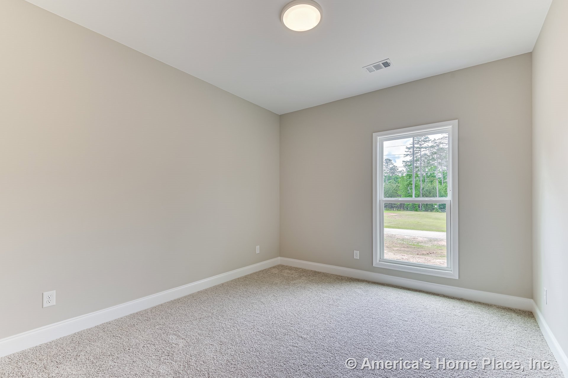 Rectangular bedroom with light beige carpet, neutral painted walls, single window with white trim, flush mount ceiling light, white baseboards, and electrical outlet.