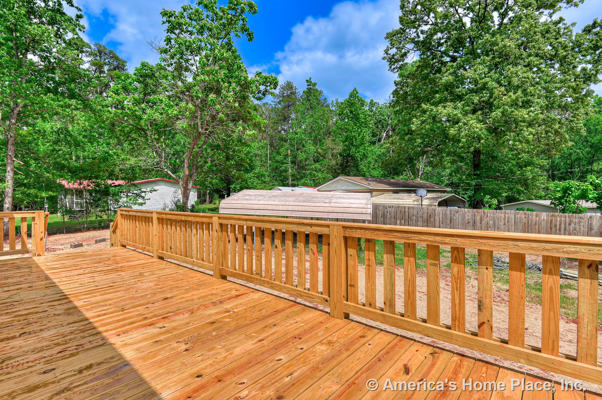 Expansive outdoor deck with natural wood plank flooring and built-in sturdy wooden railing, overlooking a fenced backyard and open exterior space.