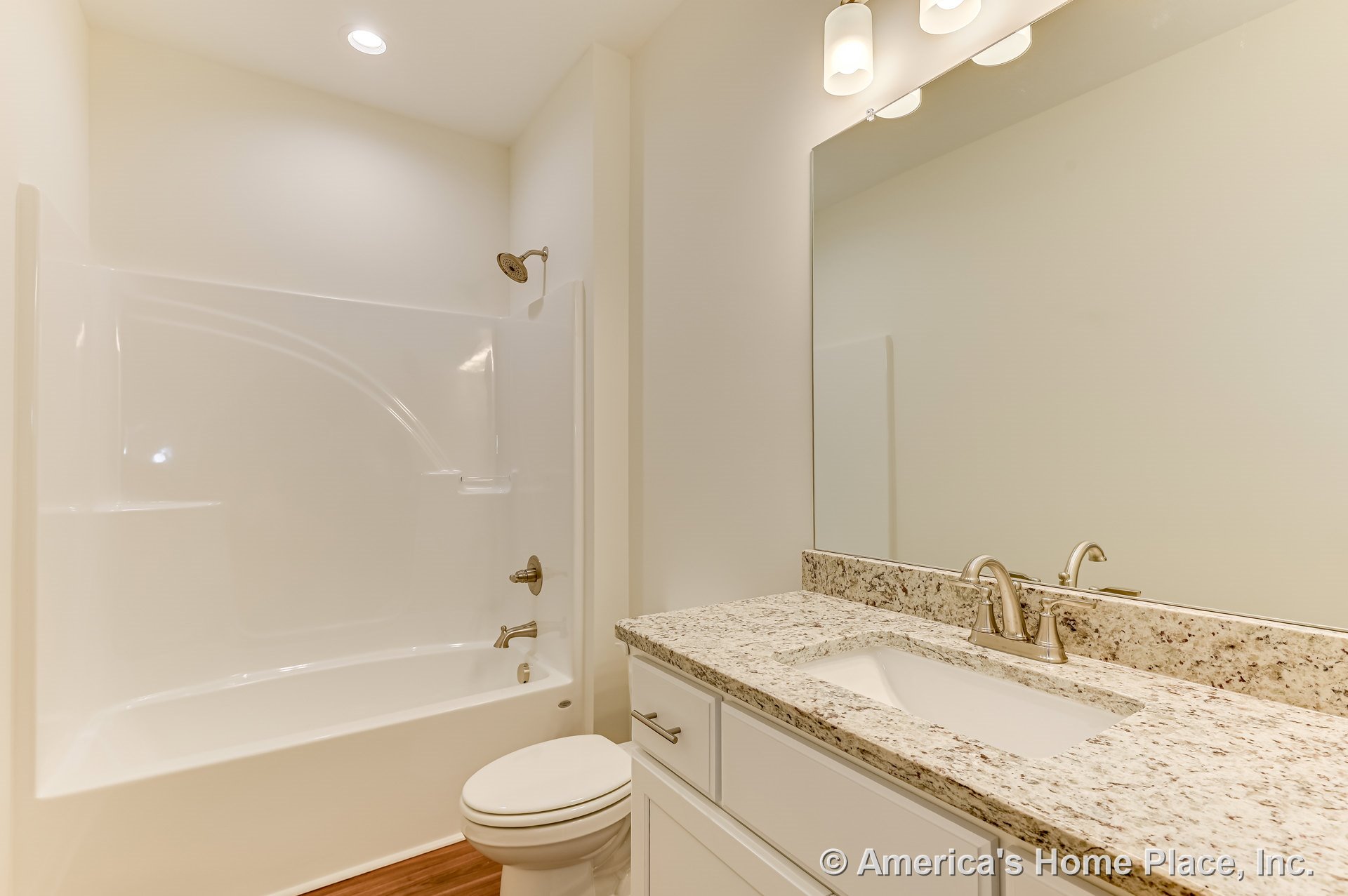 Granite vanity countertop with integrated sink, white cabinetry, chrome faucet, built-in tub and shower combination, large mirror, recessed ceiling light, wall-mounted vanity