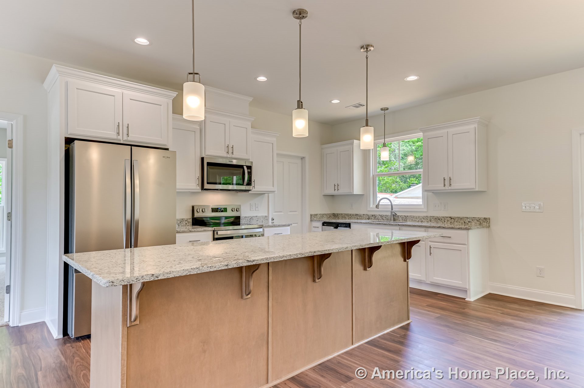 Spacious kitchen with white upper and lower cabinets, granite countertops, stainless steel refrigerator, oven, and built-in microwave, large wood-paneled island with pendant