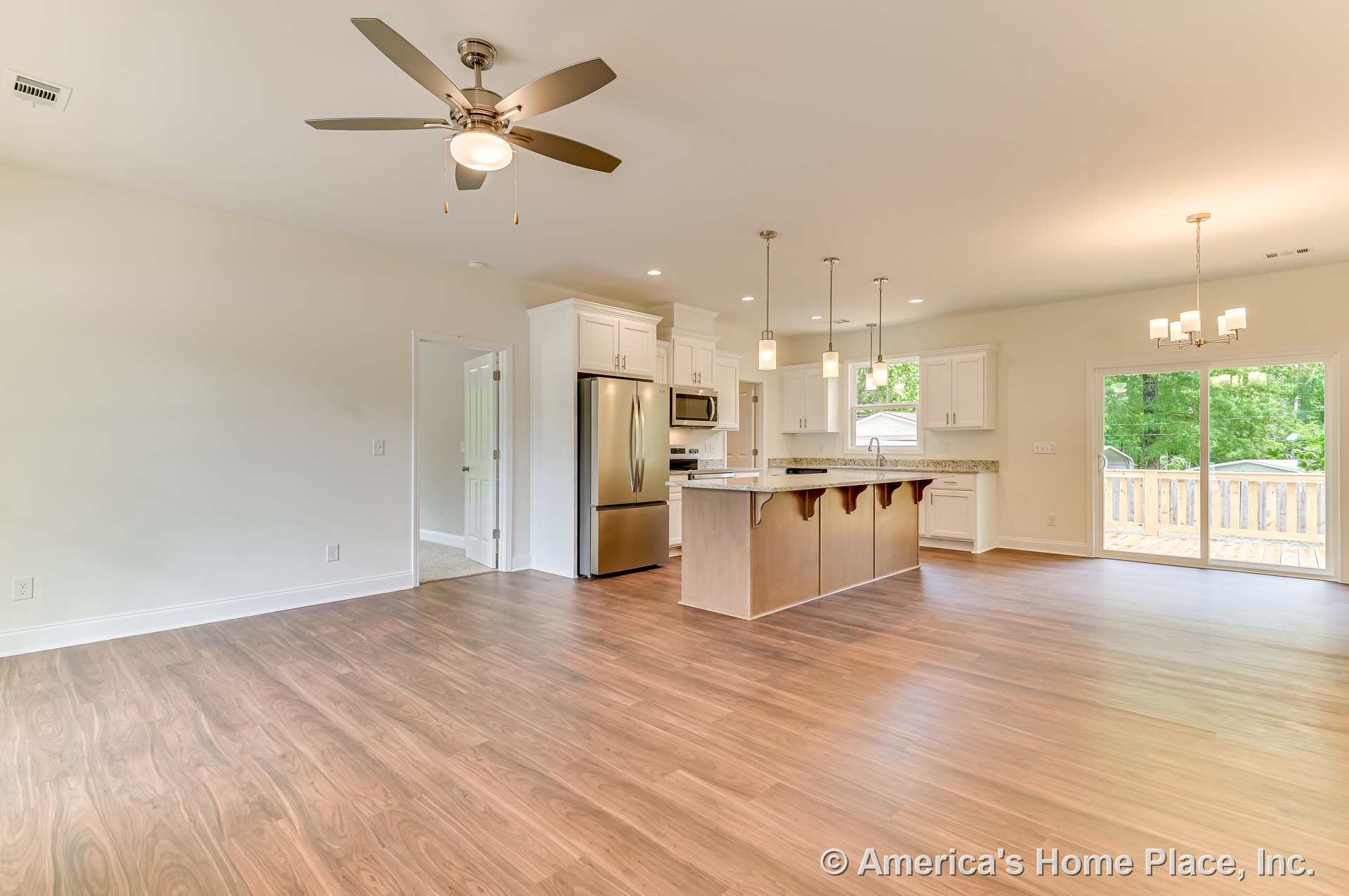 Open kitchen and living area with wood-look plank flooring, white shaker cabinets, granite countertops, stainless steel appliances, central island with pendant lighting, recessed