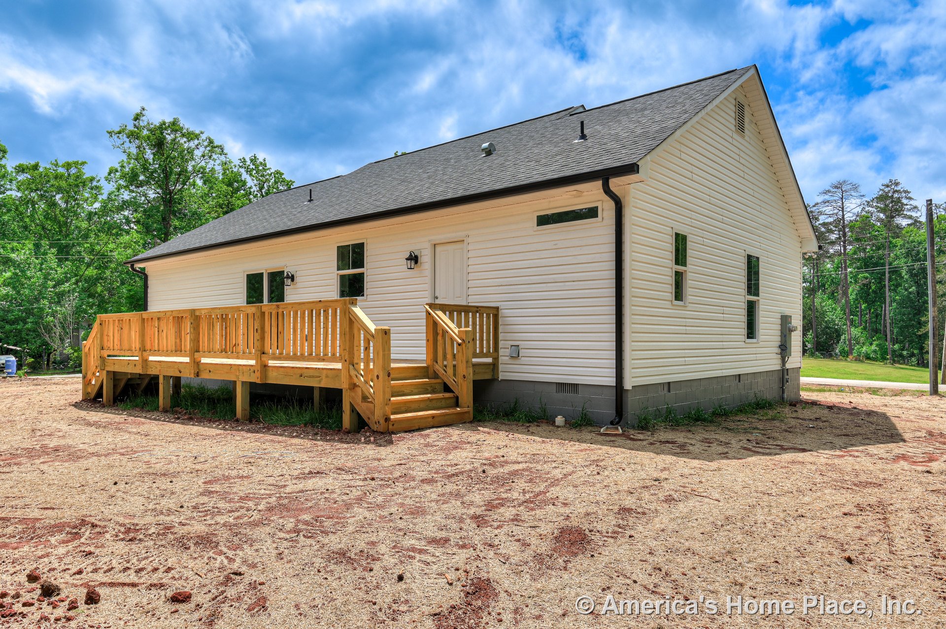 White vinyl siding exterior with multiple rectangular windows, gable roof with asphalt shingles, wooden front porch featuring railings and steps, concrete block foundation, and
