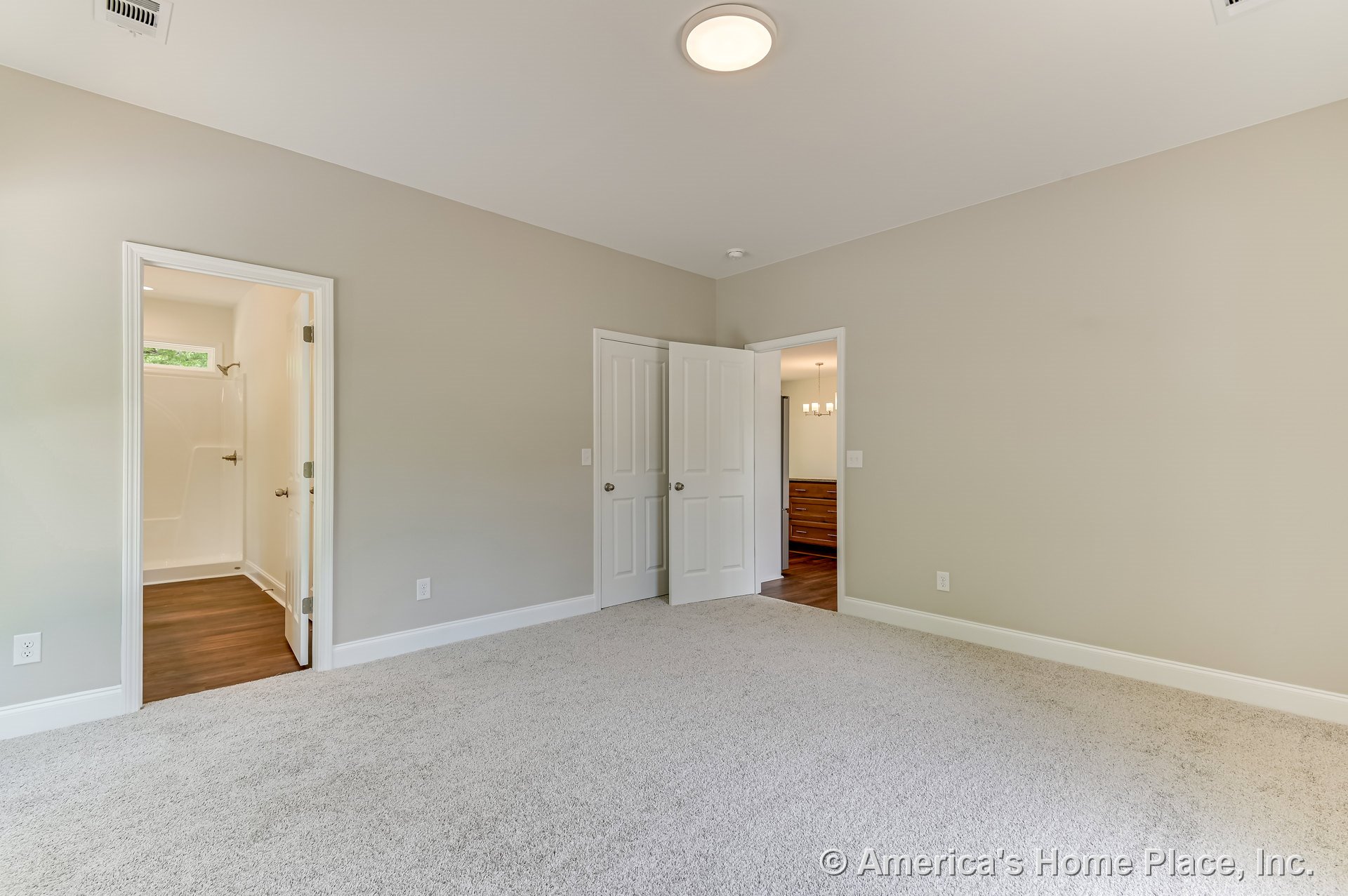 Bedroom with light carpet flooring, neutral painted walls, white baseboards, flush ceiling light, and two white paneled doors providing access to a hallway and a bathroom with a