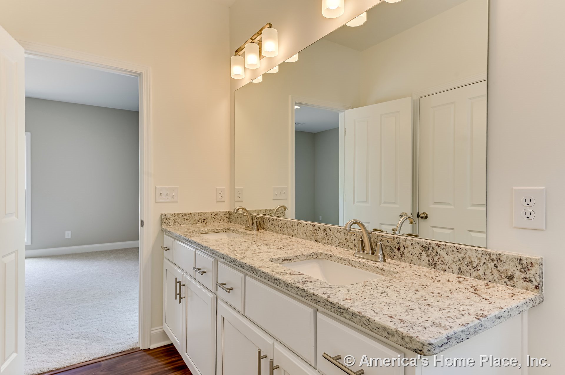Double vanity with granite countertop, two undermount sinks, white shaker cabinets, large wall mirror, brushed nickel faucets, built-in vanity lighting, neutral painted walls, and