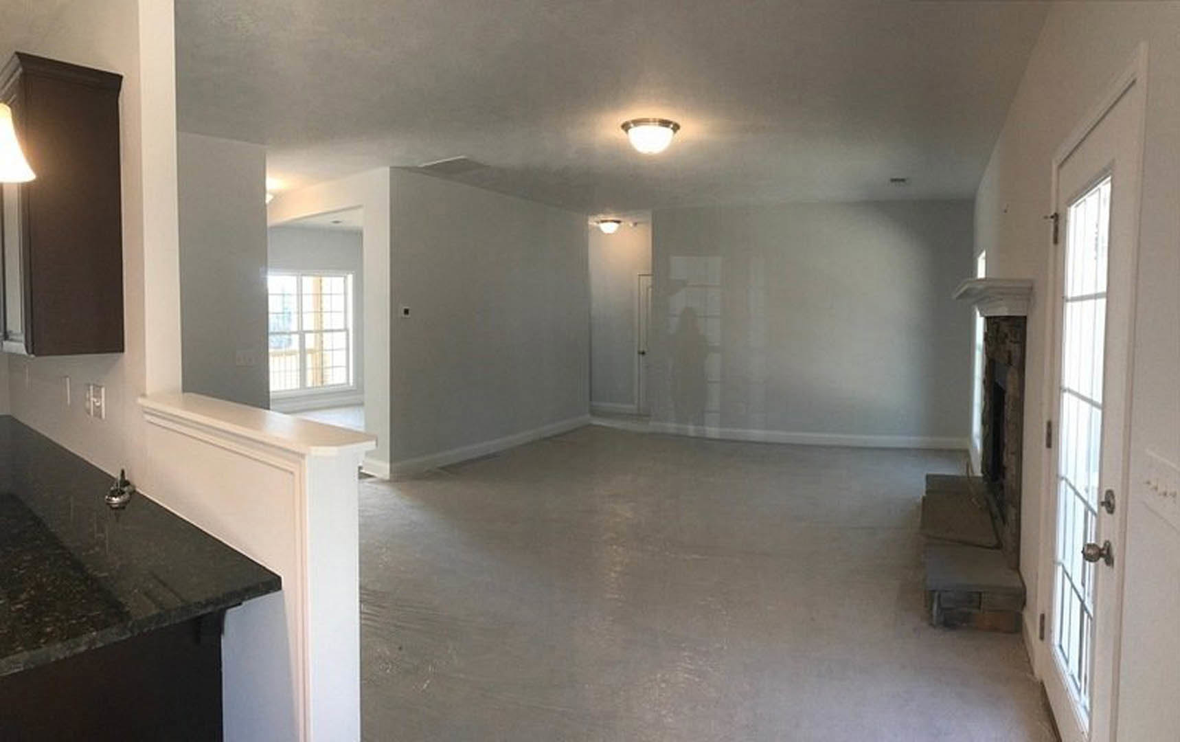Open living area featuring a white tile floor, modern staircase with metal railing, light gray couch, black countertop, white plaster walls, and wall-mounted light fixture.