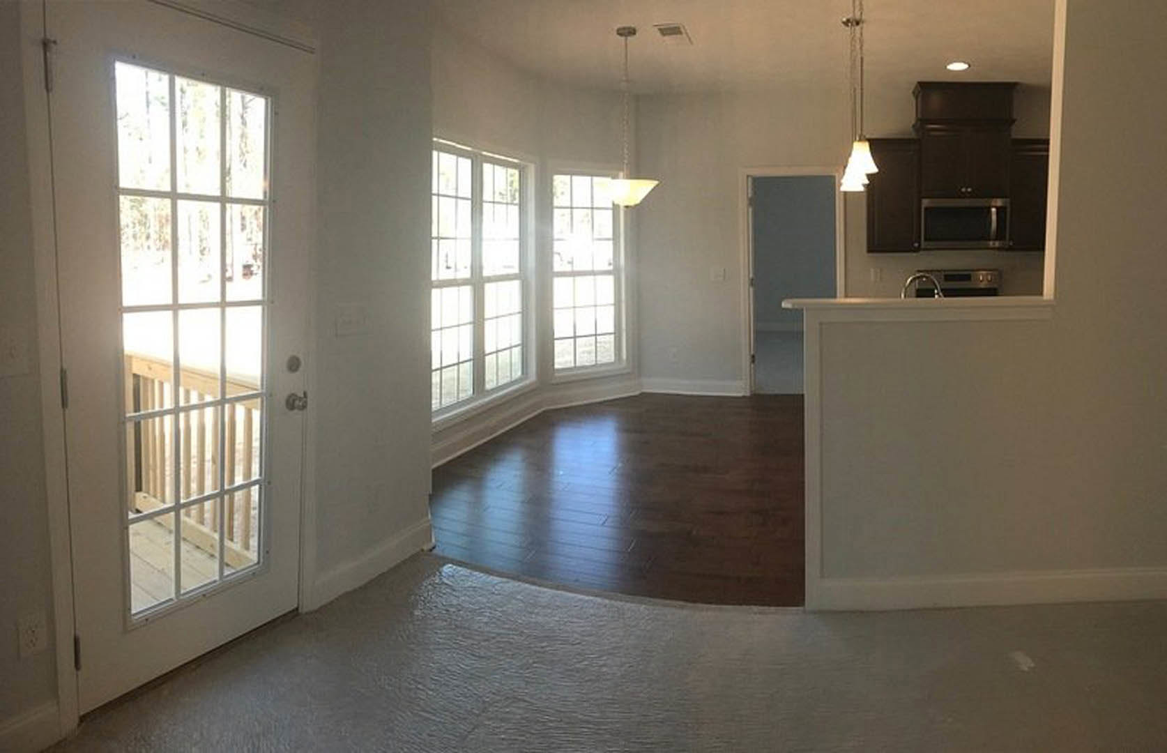 Open-concept kitchen with white cabinetry, hardwood flooring, glass-paneled door, and a white dining table under pendant lighting