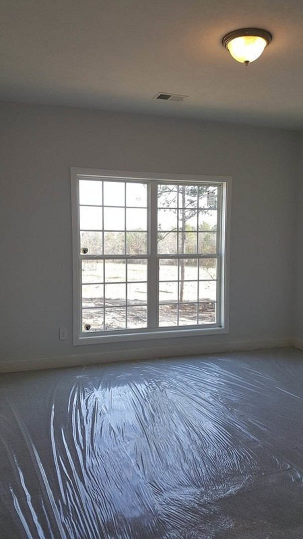 Room with multi-pane window overlooking trees, plastic sheeting covering the floor, plaster walls, ceiling light fixture, and window blinds