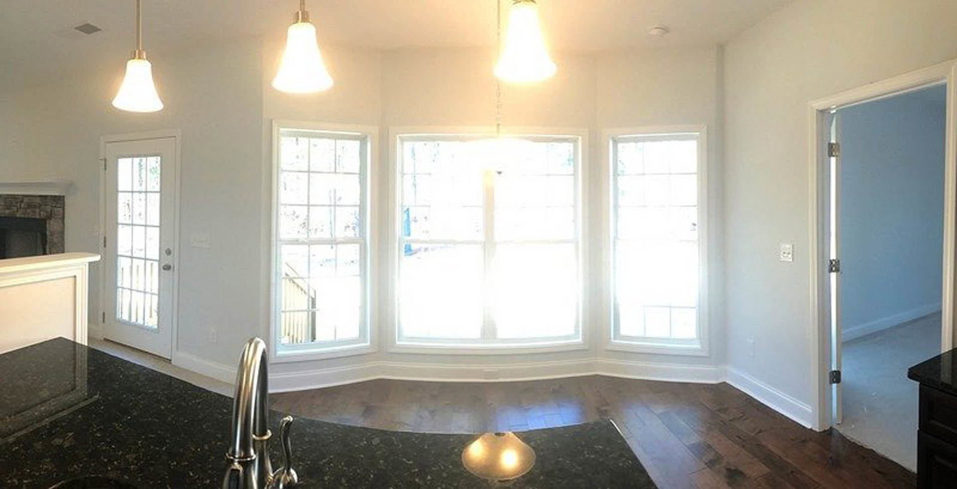 Marble countertop with chrome faucet in a bright room featuring large windows, white cabinetry, glass-paneled door, and ceiling light fixture