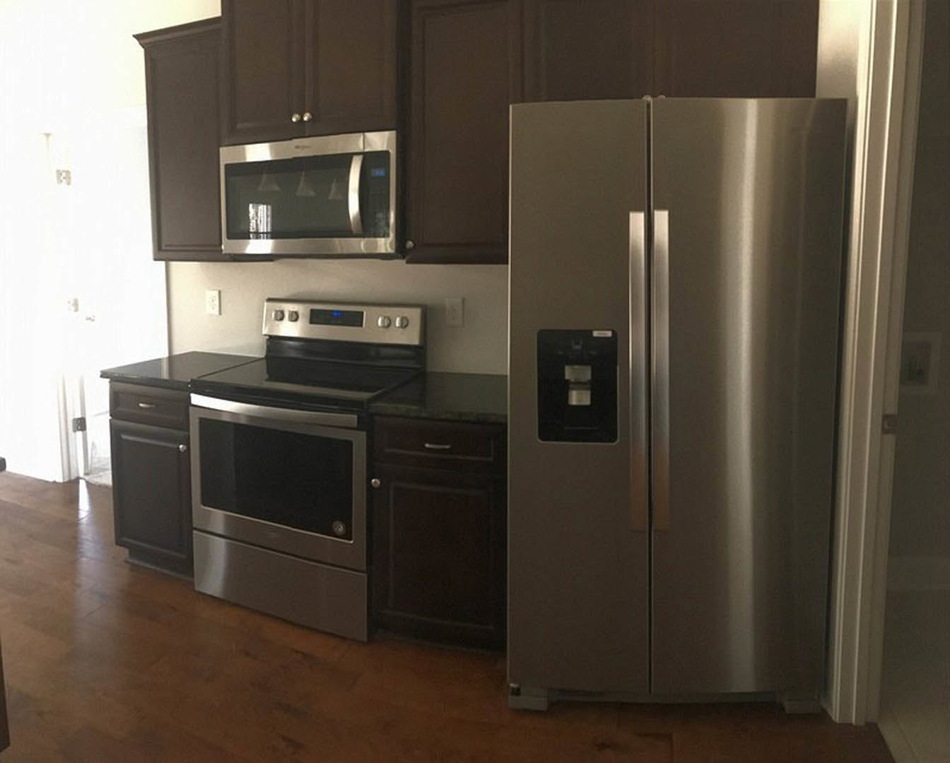 White kitchen with shaker cabinets, stainless steel refrigerator and stove, built-in microwave above oven, light stone countertops, and tile backsplash