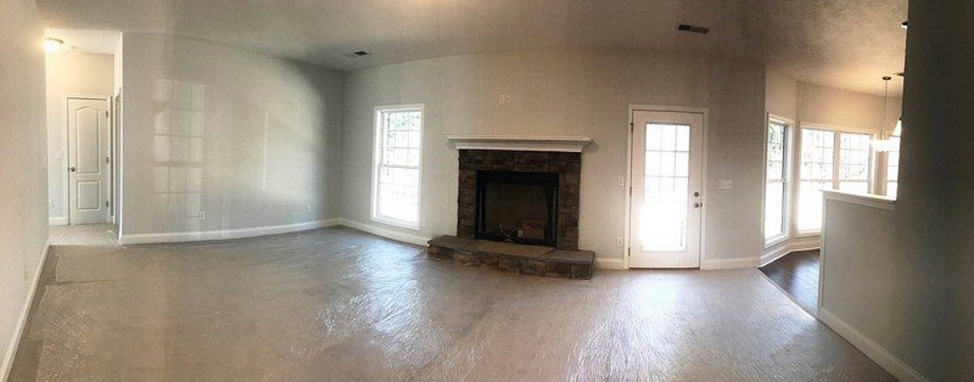 Living room with plaster walls, concrete floor, white framed window, modern fireplace with firewood box, and white door featuring a silver handle and glass panel.