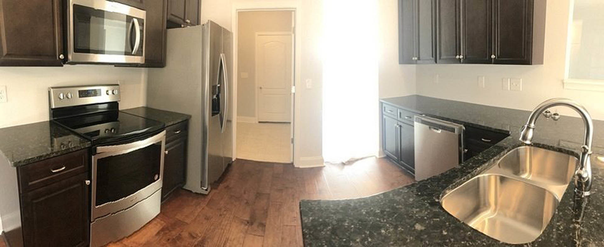 Modern kitchen featuring white cabinetry, stainless steel appliances including refrigerator, oven, microwave, and dishwasher, open door leading to adjacent room, quartz