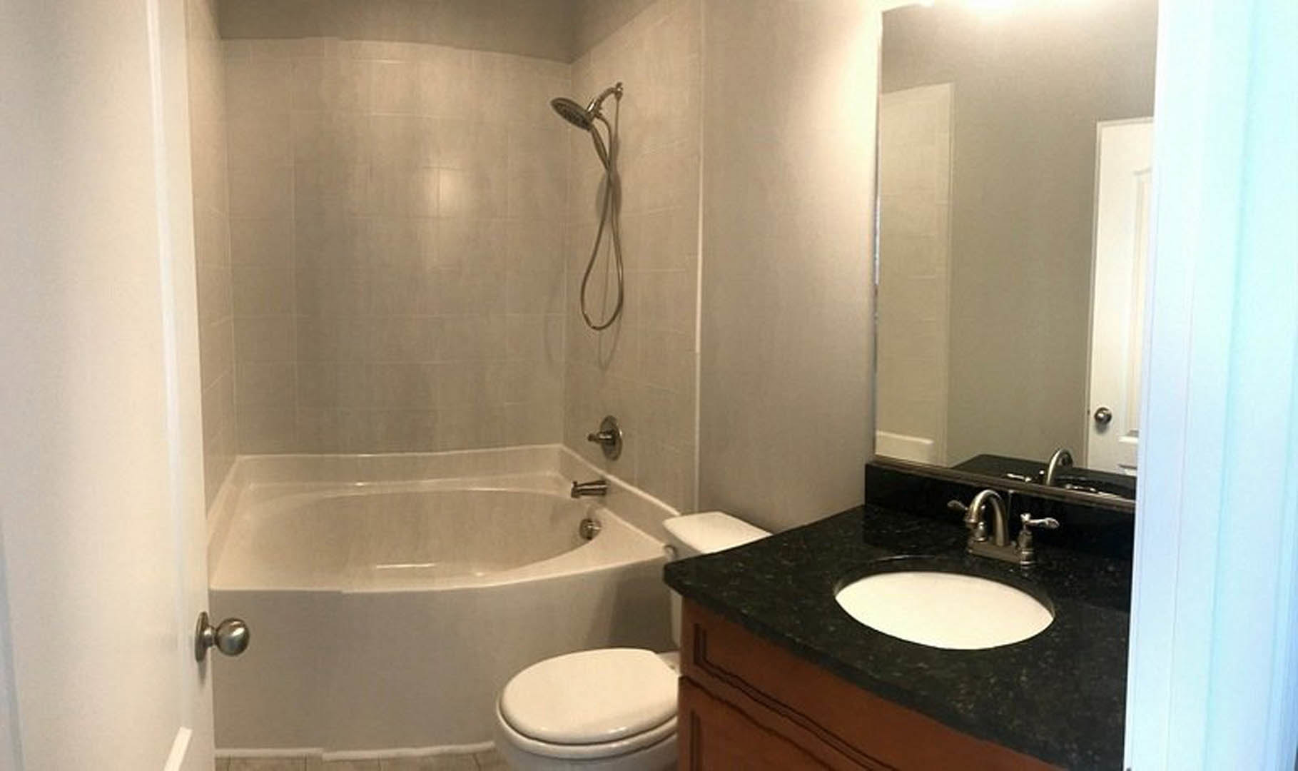 Modern bathroom featuring freestanding white bathtub, rectangular vessel sink on wood vanity, large wall mirror, light gray tile flooring, and chrome fixtures.