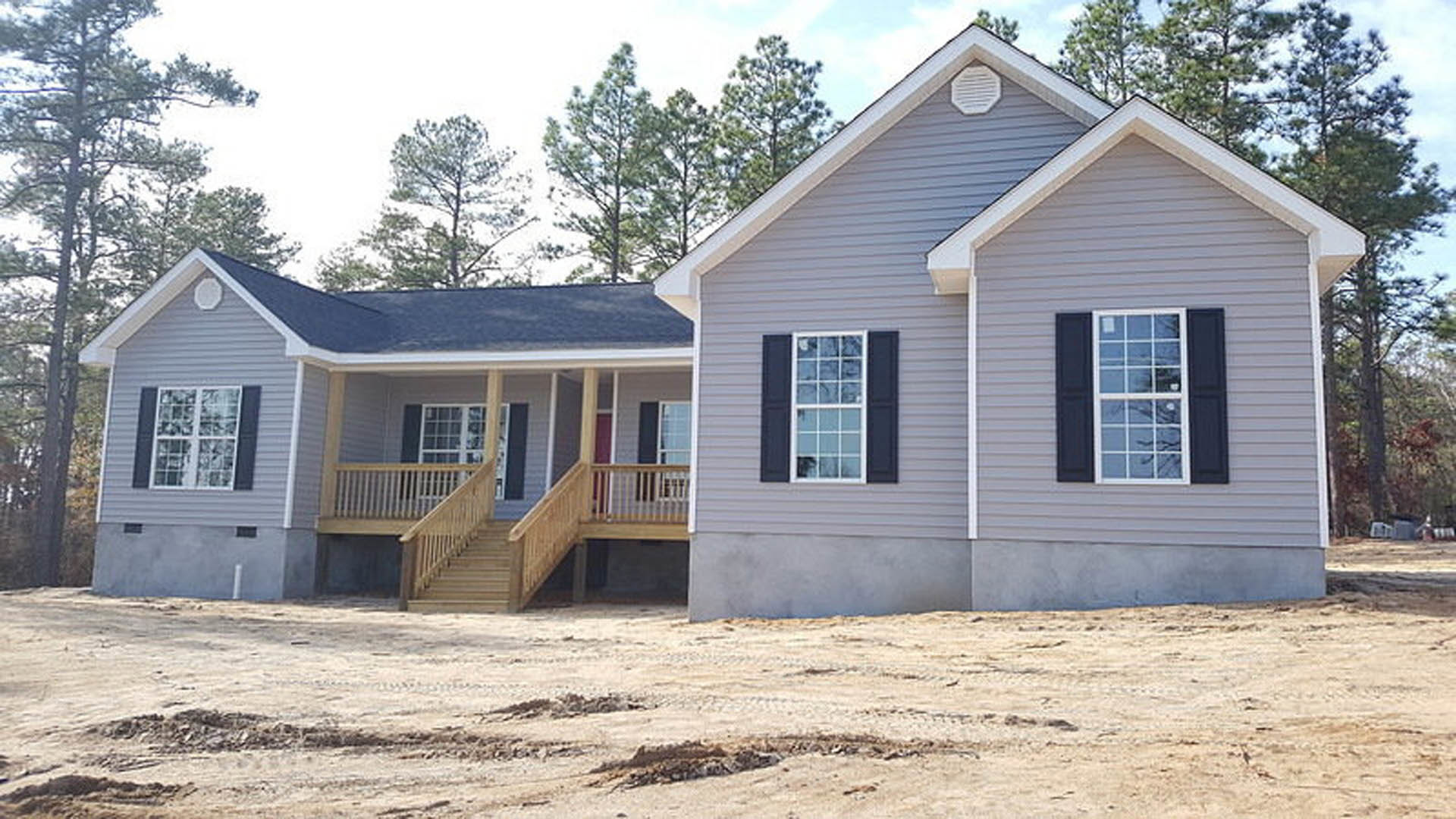 Two-story home with white siding, black shuttered windows, covered front porch, wooden steps, and landscaped yard with trees.