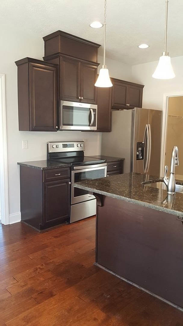 Kitchen with dark wood cabinets, stainless steel refrigerator, built-in microwave, countertop oven, and dark brown wooden flooring