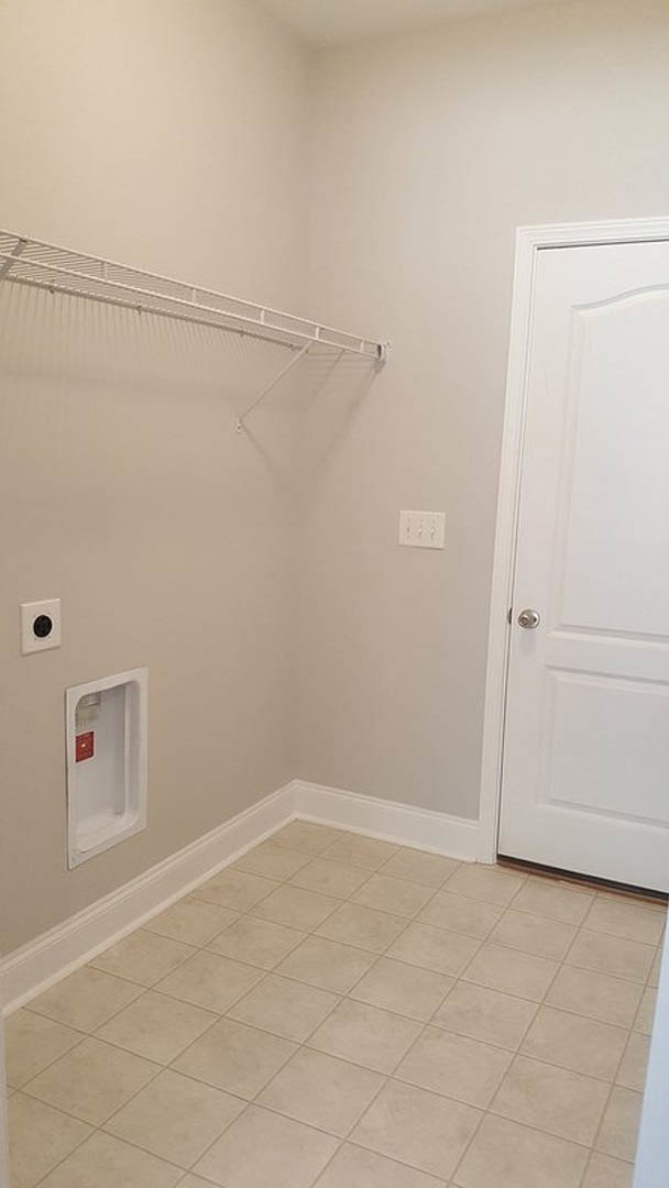 White clothes rack beside a white wall with a red sign, tile flooring, white railing, and shelf in a residential room.