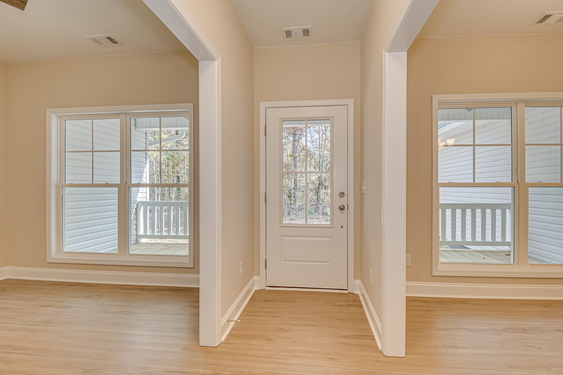 Hallway with wood flooring, white walls, white door with glass panel, large window showing trees outside, white railing along the side