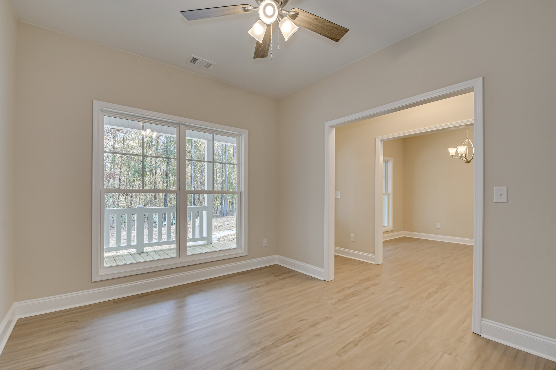 Ceiling fan with lights above wood flooring and white trim, large window overlooking deck and trees