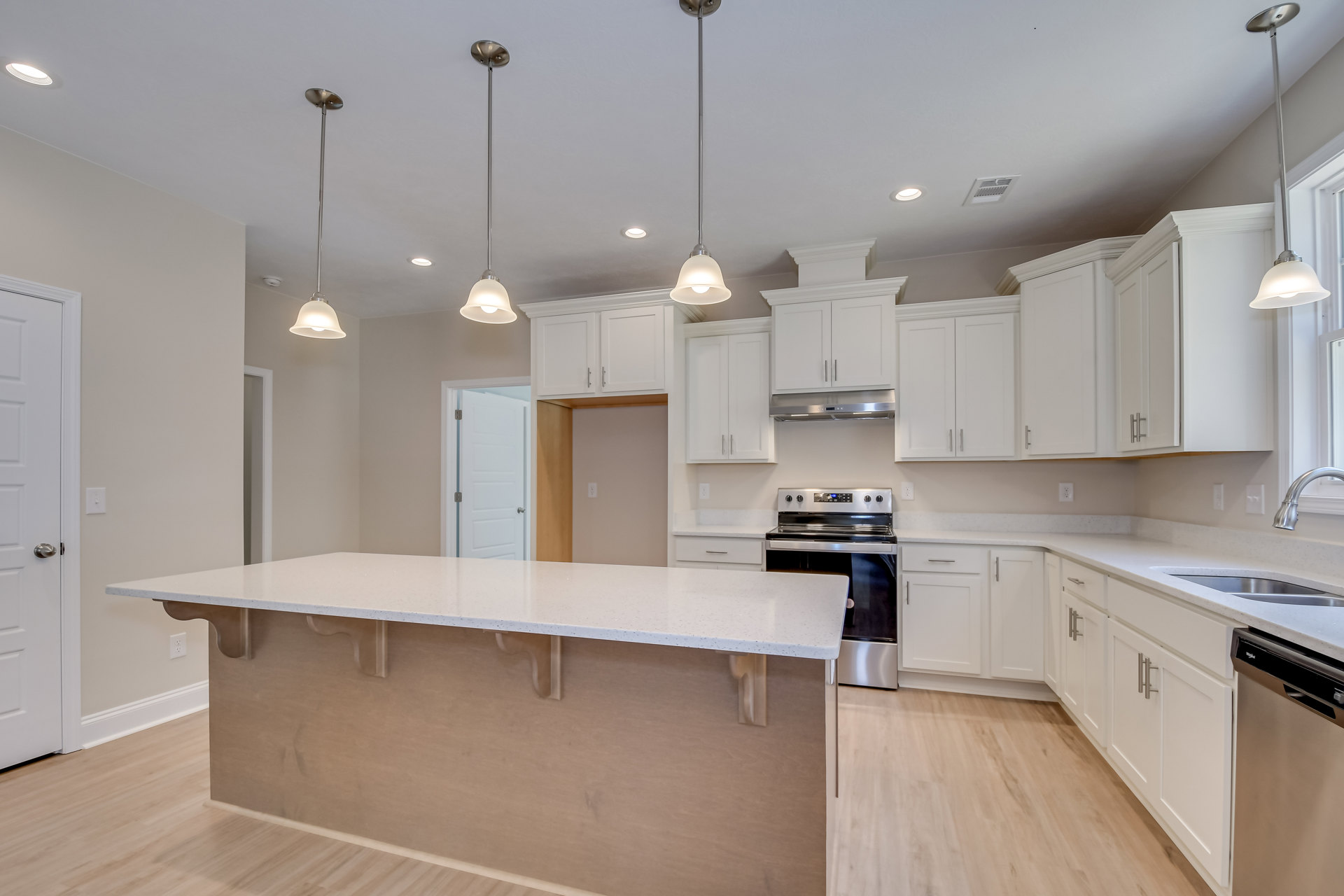 White kitchen with shaker cabinets, spacious central island with quartz countertop, stainless steel stove, undermount sink, silver hardware, light wood flooring, and recessed