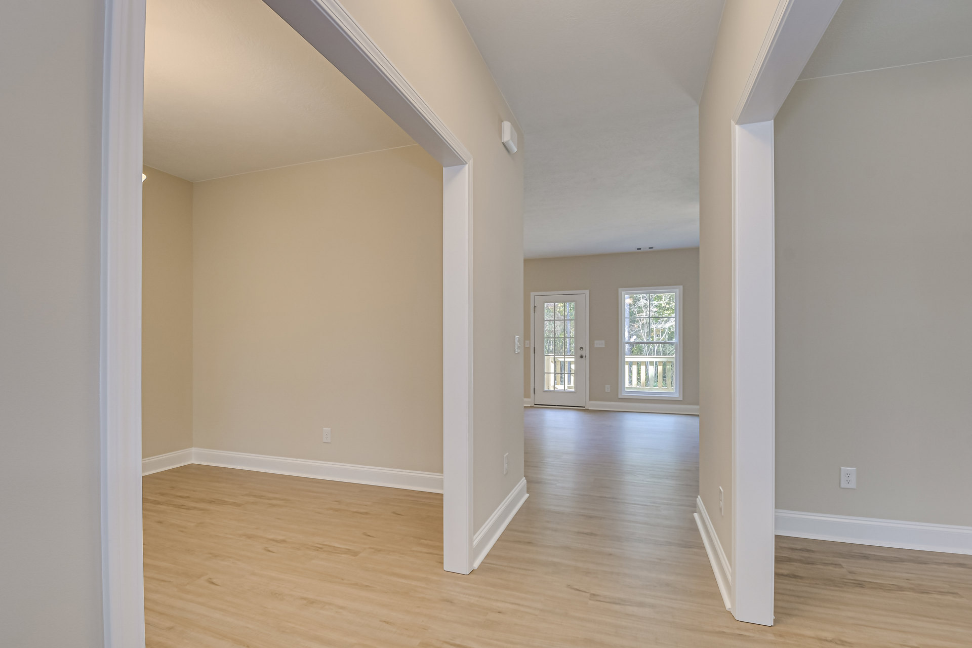 Hardwood floor with white trim in a room featuring white walls, a glass-paneled door, two doors with windows, and a window overlooking trees outside